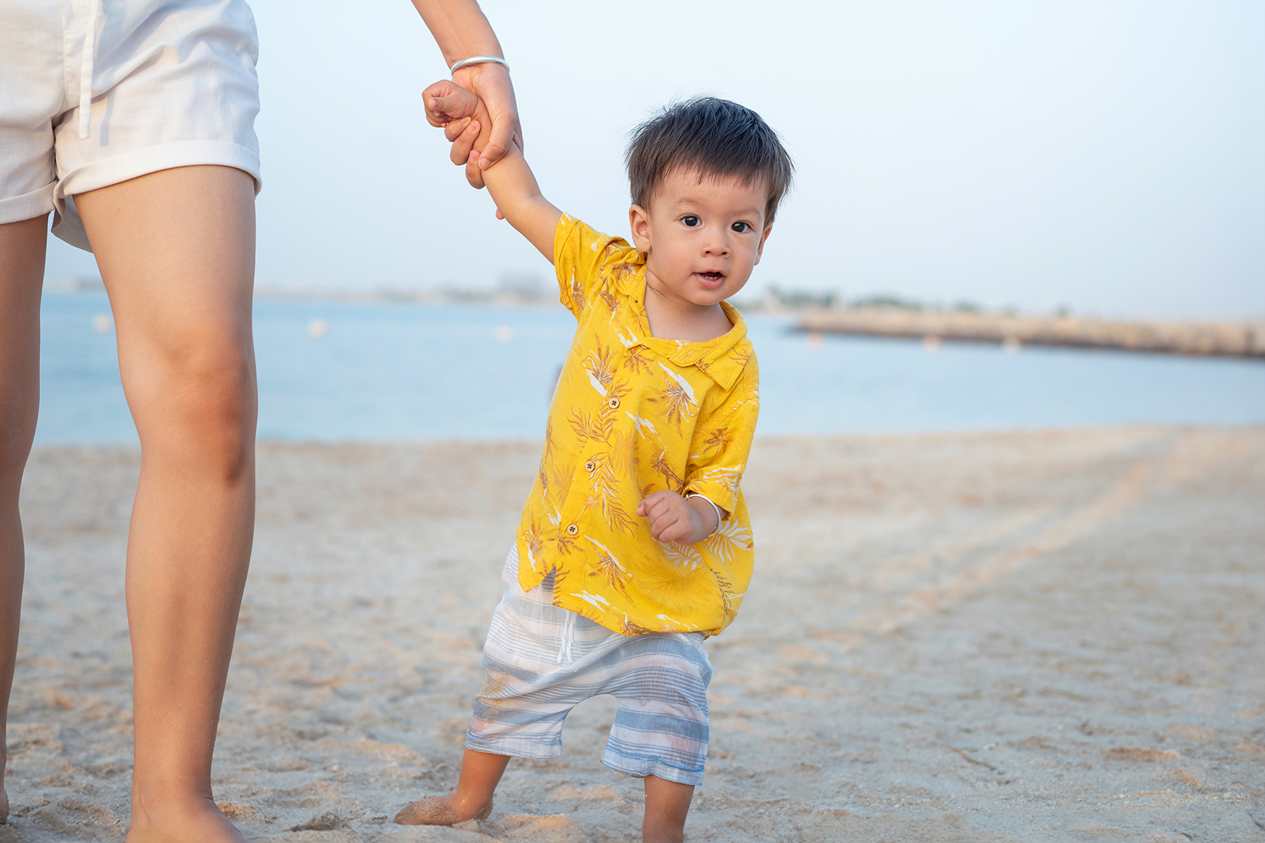 Child walking on the beach holding hands with their parent.