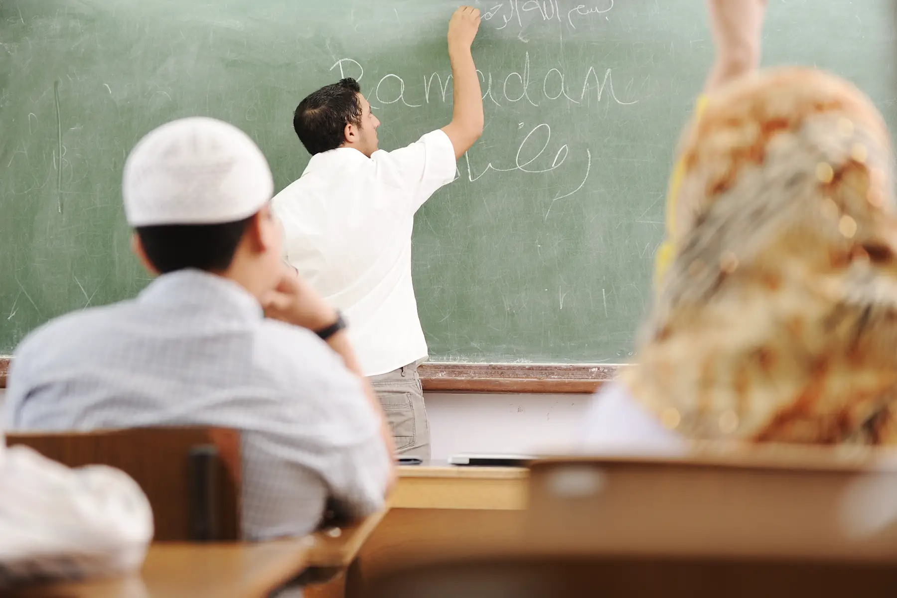 A teacher writes on the chalkboard in an Arabic lesson