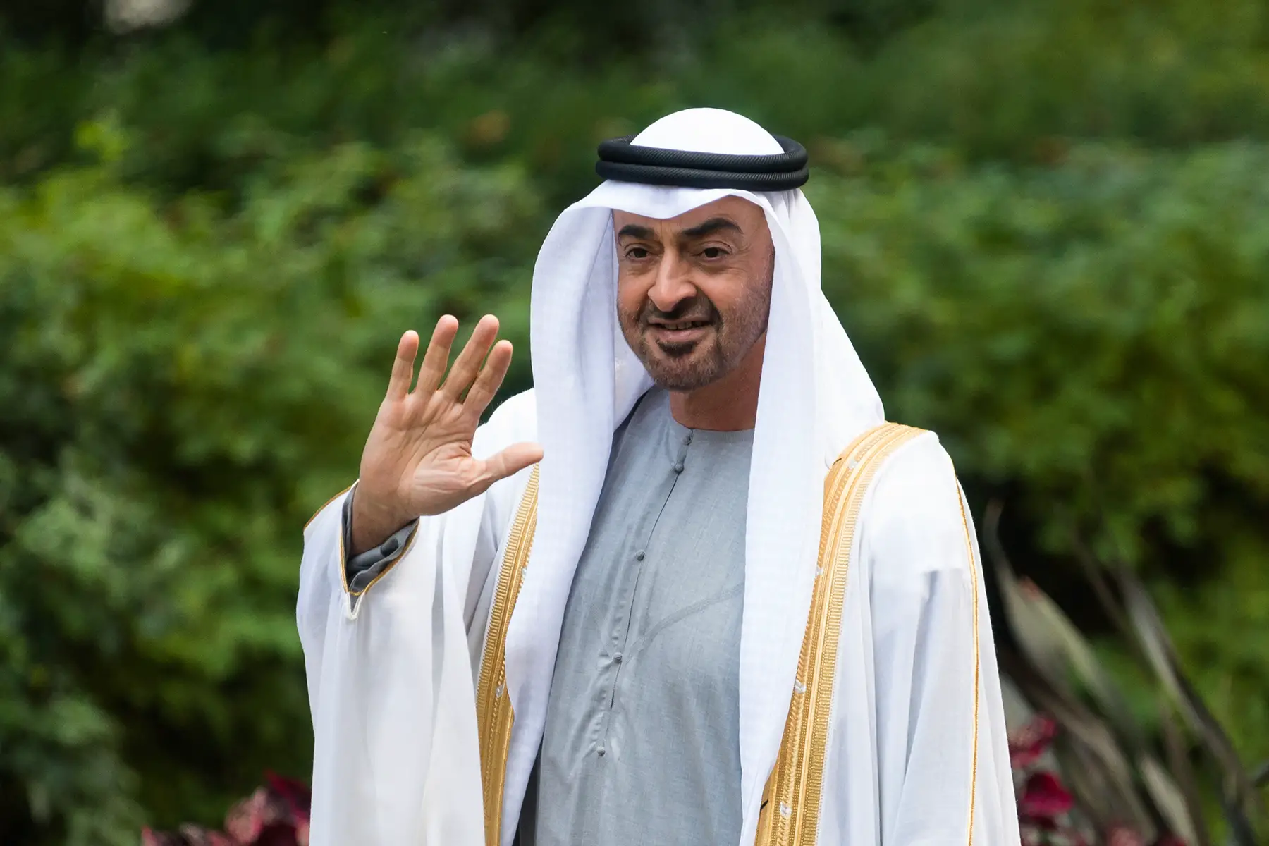 Crown Prince Sheikh Mohammed bin Zayed Al Nahyan waving while standing in front of some greenery