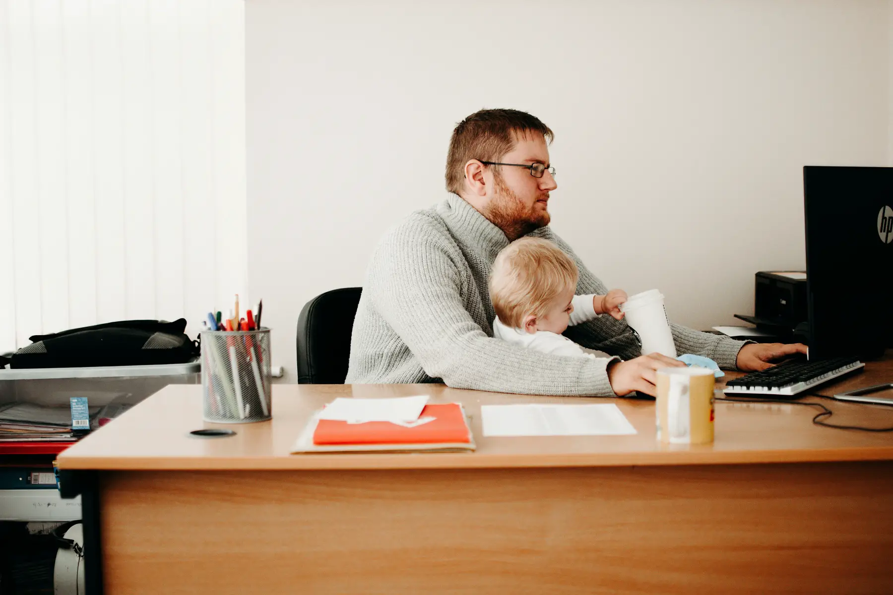 Dad working on computer with baby on lap, in office