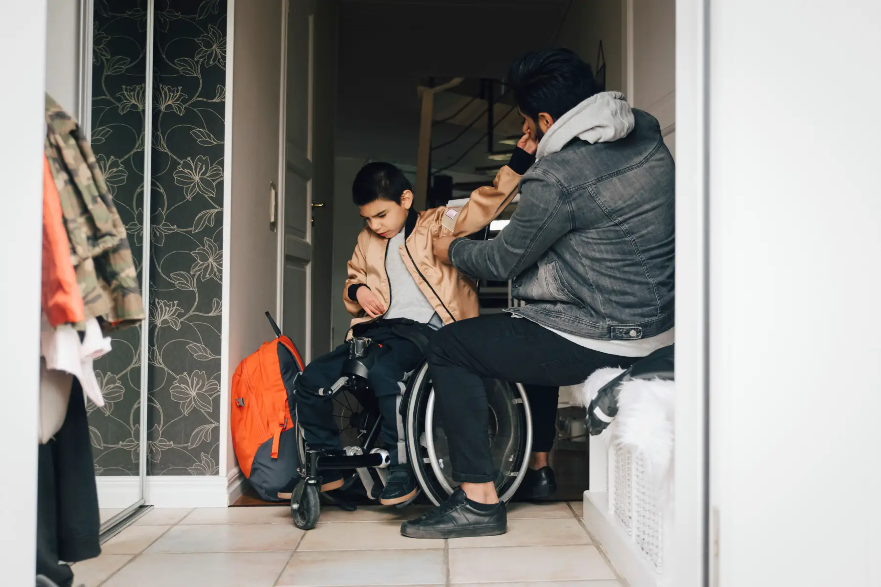Dad helping son with disabilities (using a wheelchair) putting jacket on