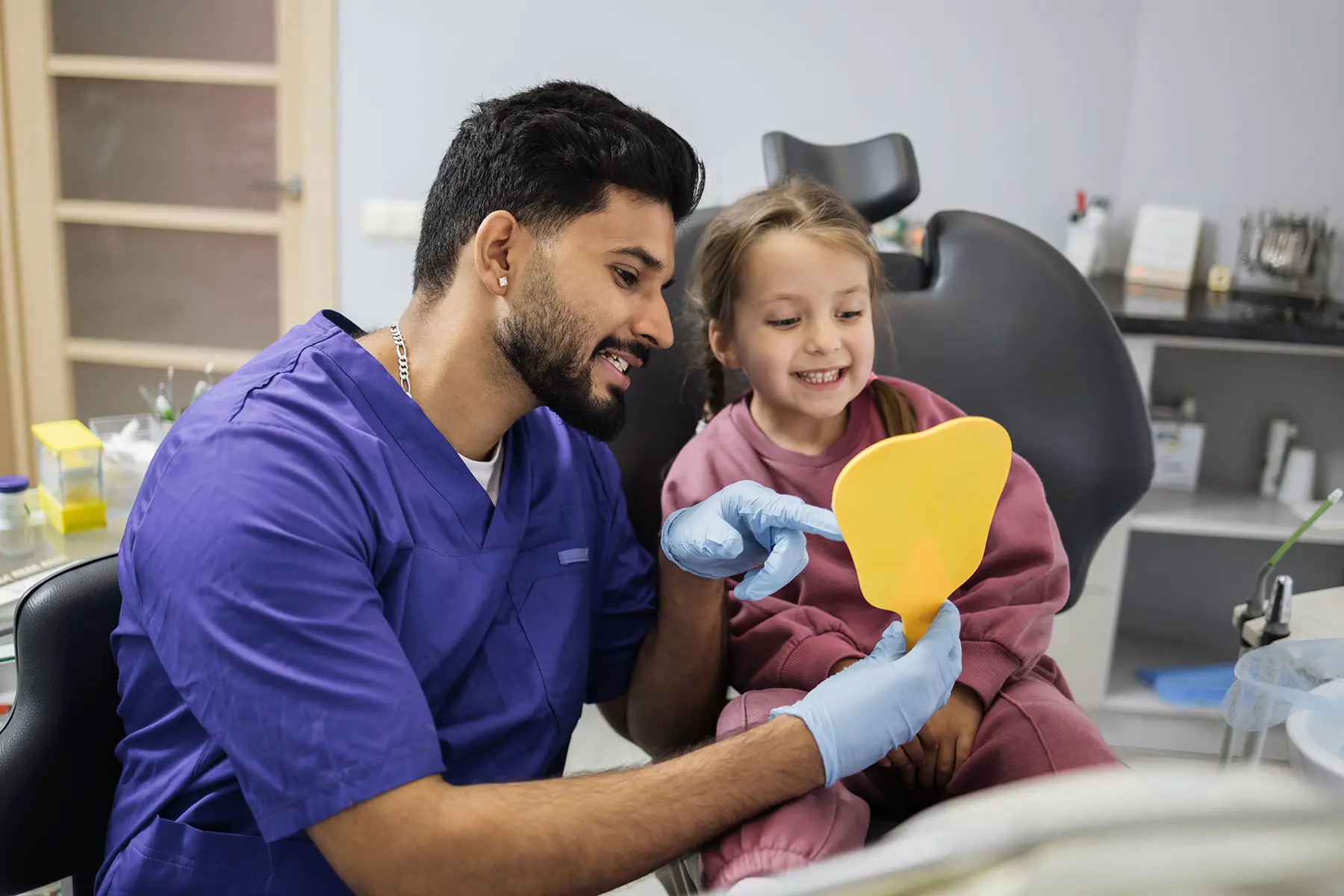 Dentist holding up a mirror for a young girl to smile in.