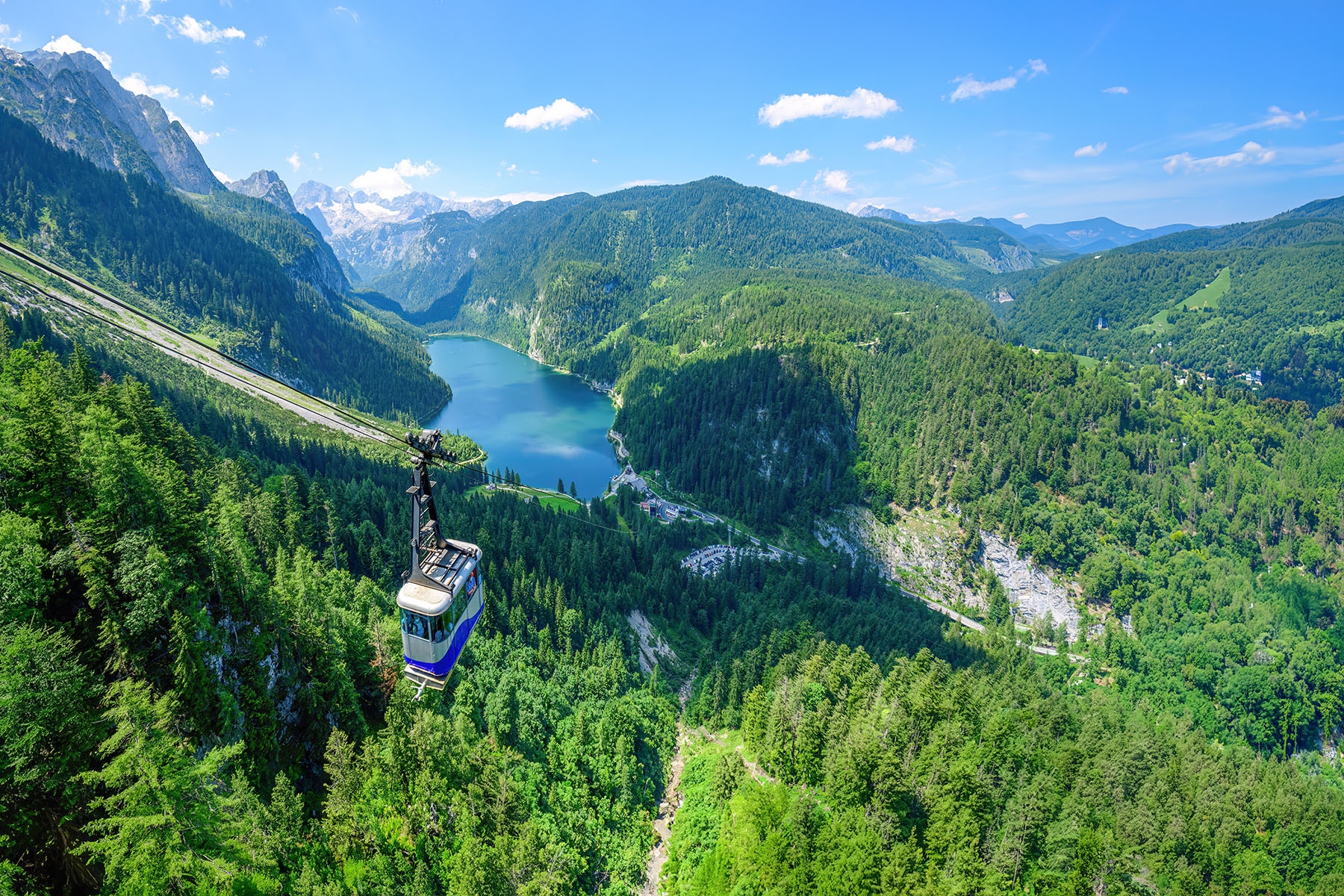 A cable car goes up and down across green mountains and a lake in Austria, Salzkammergut