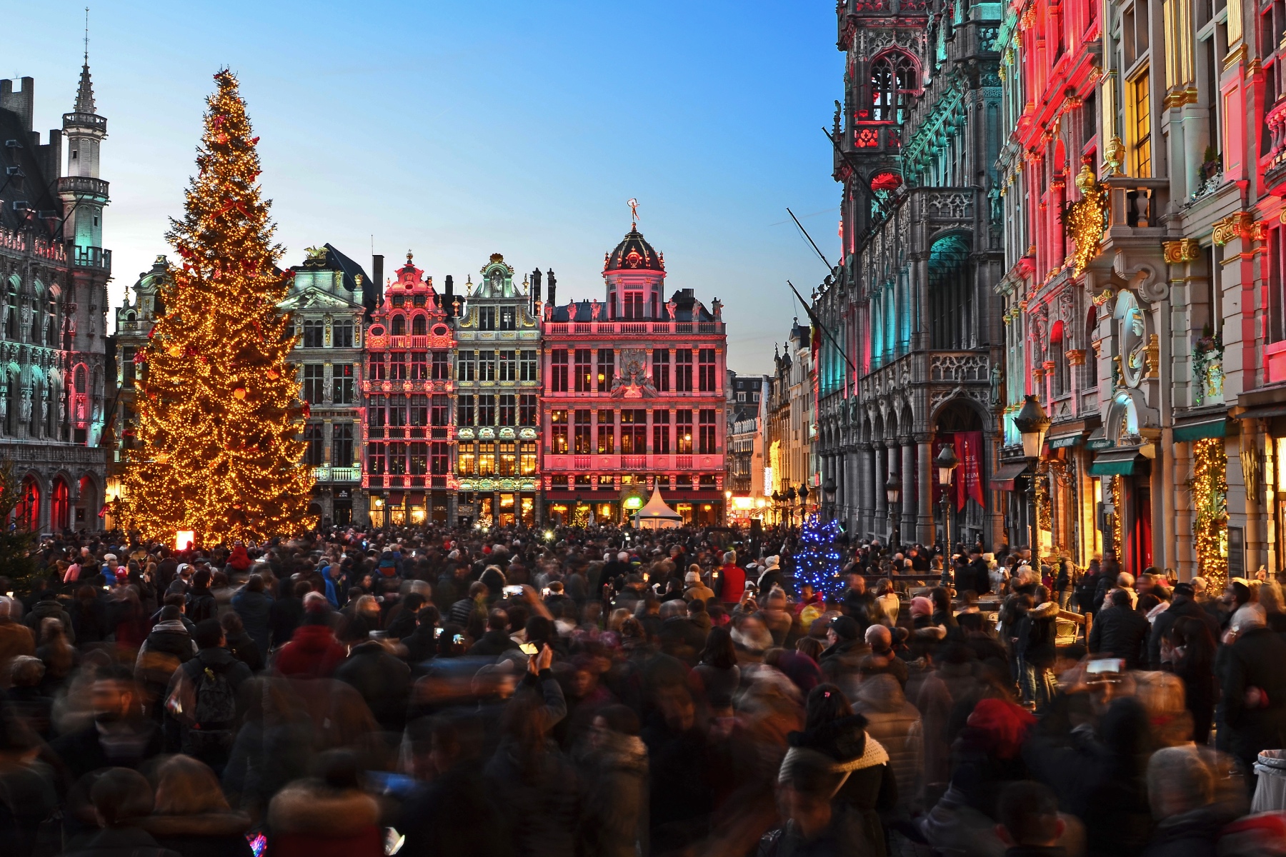 Christmas celebrated outdoors with crowds of people in Grand Palace, Brussels. The buildings in the square are illuminated with colourful lights