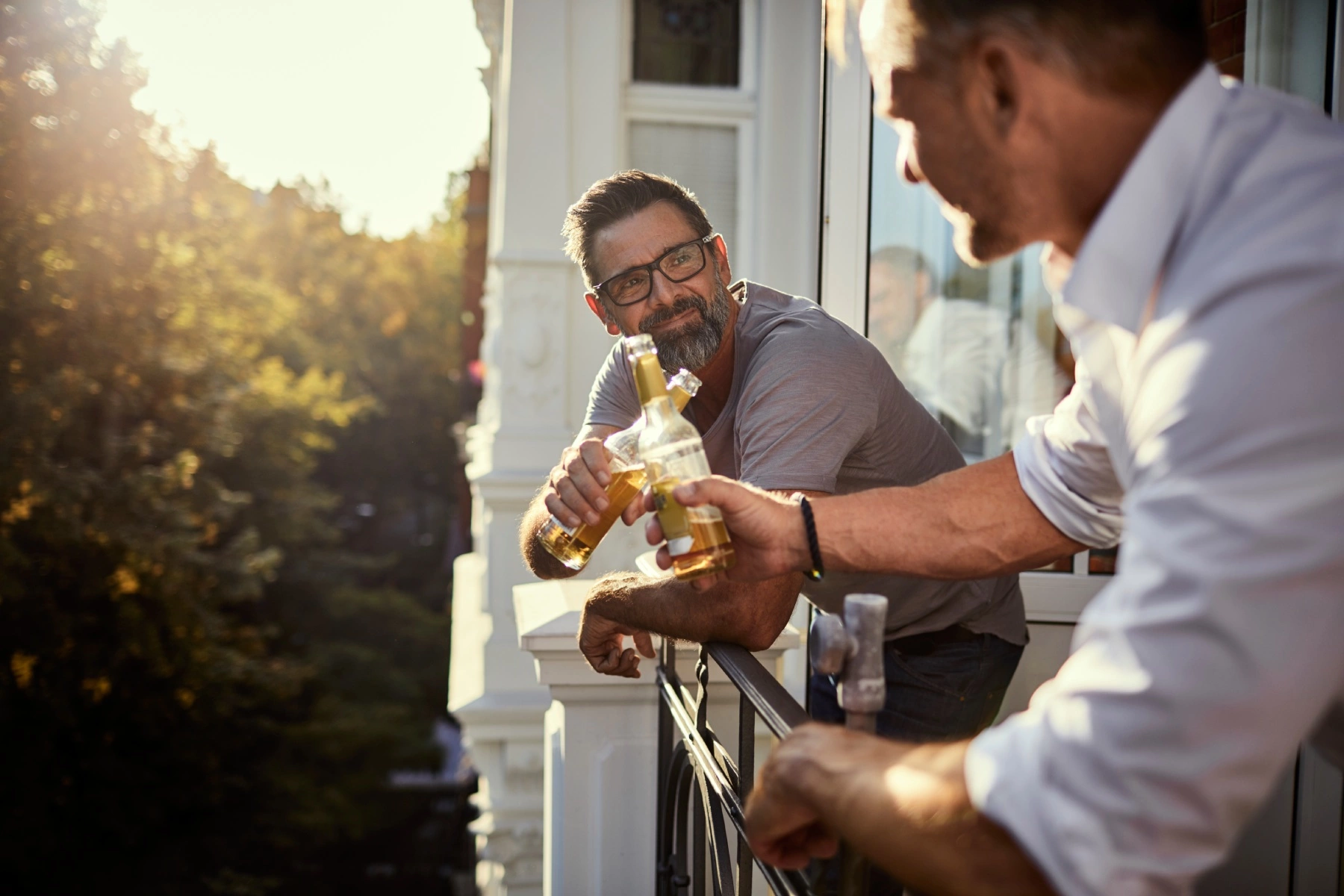 two men dressed in smart work clothes having a beer and a chat on a balcony on a sunny day