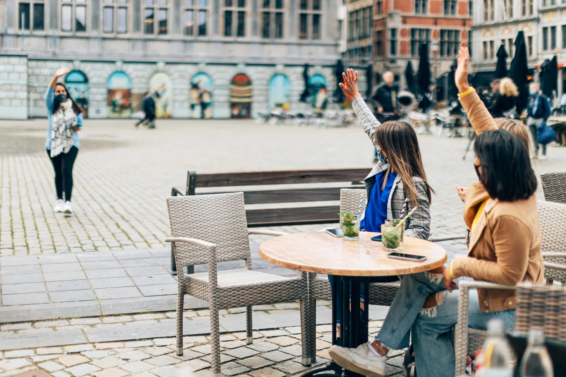 Group of friends waving 'hello' to each other at an outdoor terrace in Antwerp.