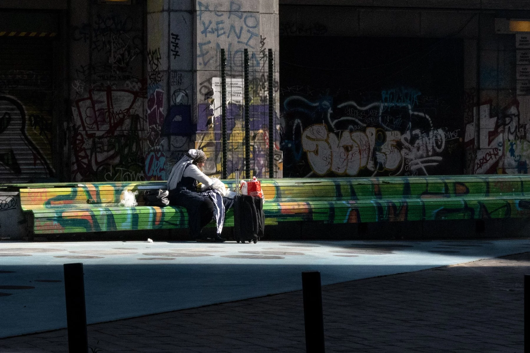 Female resident with a suitcase sitting on a bench in Brussels, not sure if she is staying or going.