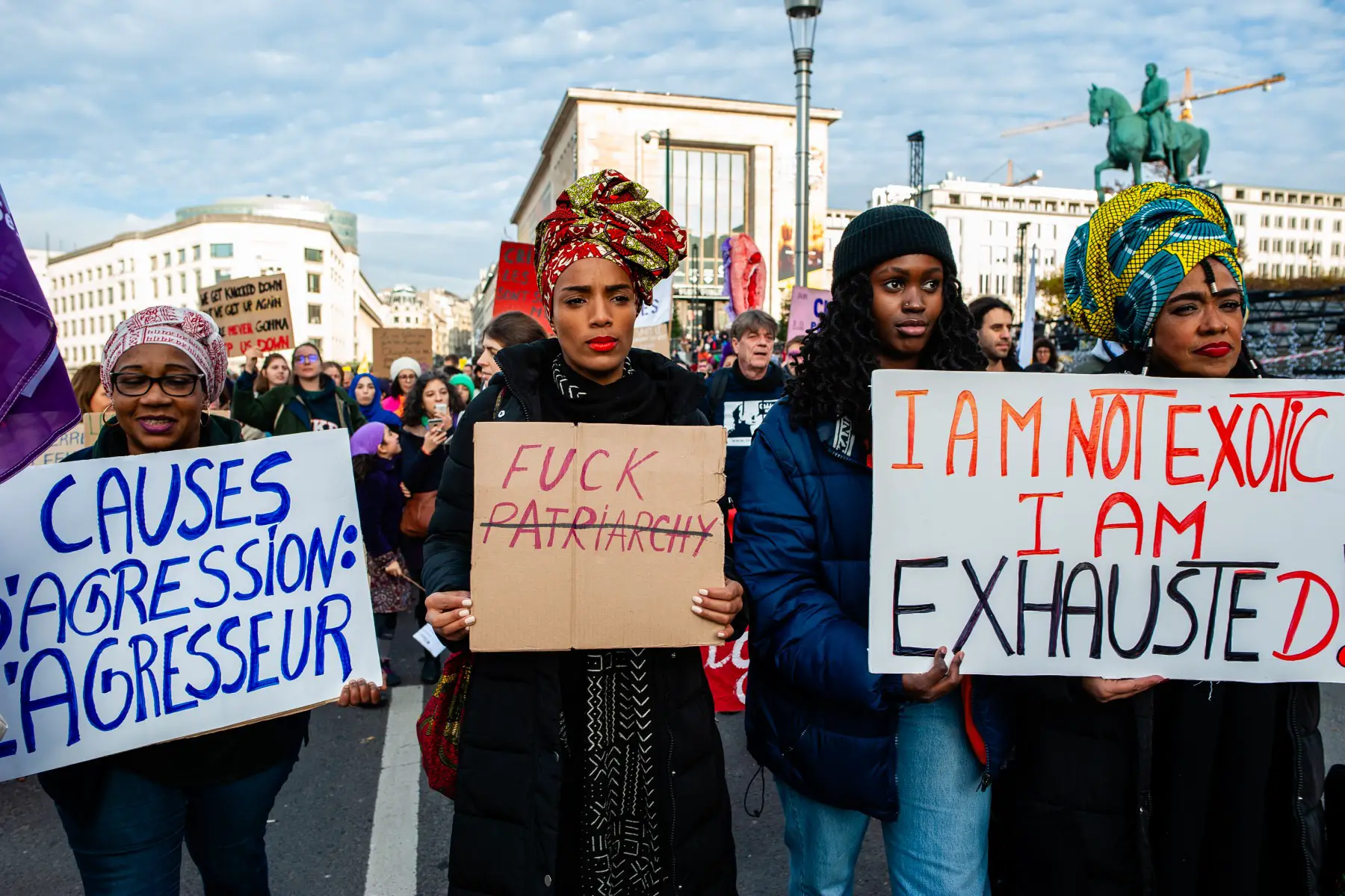 Four women of color marching during the 2019 'Stop Violence Against Women' demonstration In Brussels, their signs reading: 