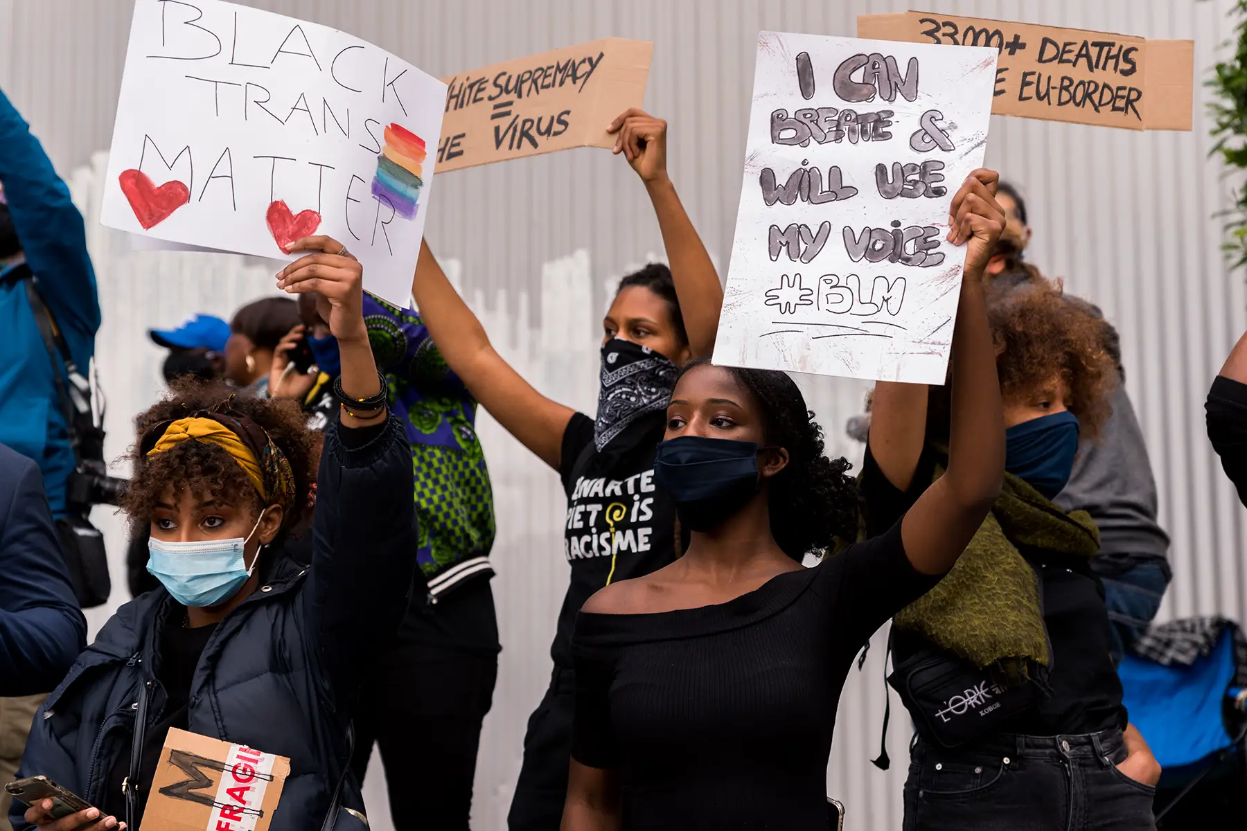 A group of people standing at a Black Lives Matter protest. They are holding signs with slogans such as 'I can breathe and use my voice #BLM' and 'Black trans matter.' 