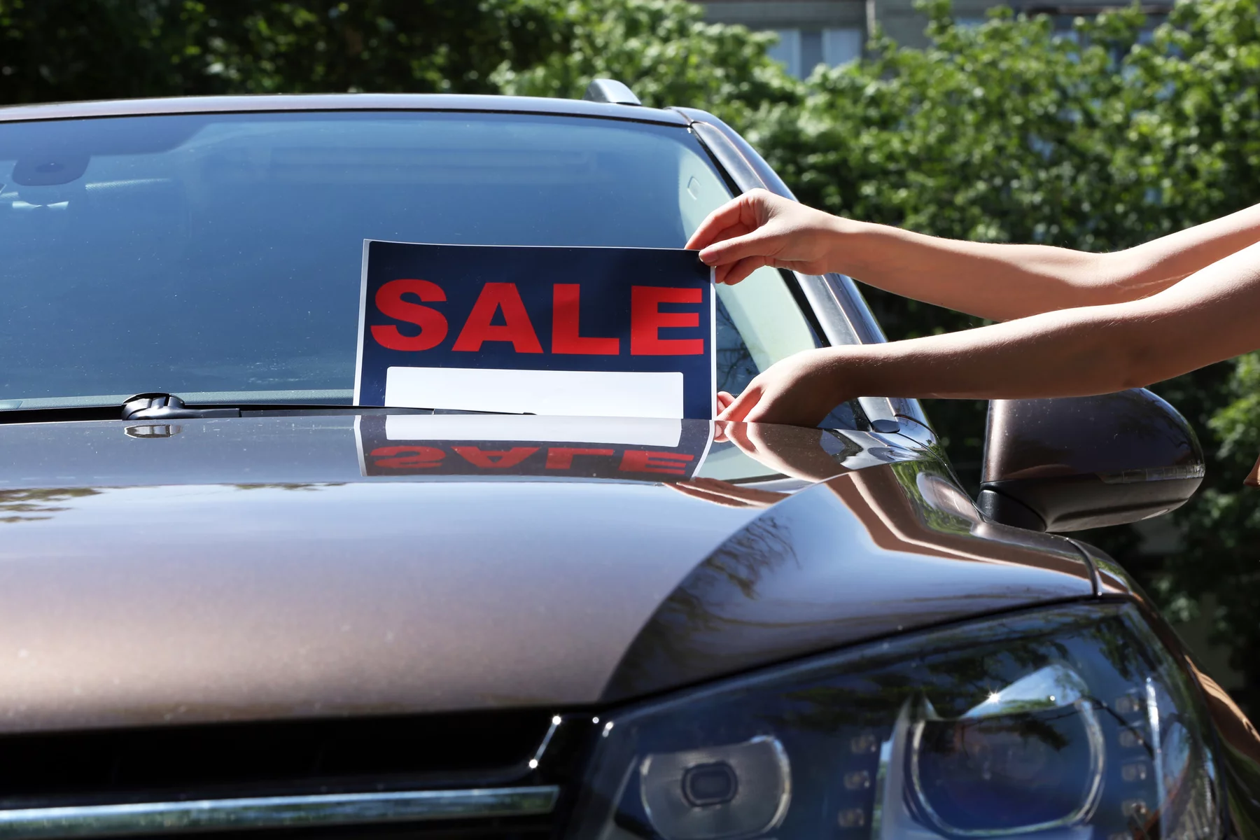 person placing for sale sign on a car