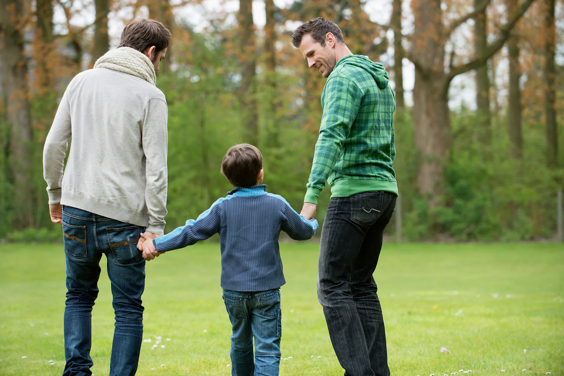 A boy walking with his dads in a park