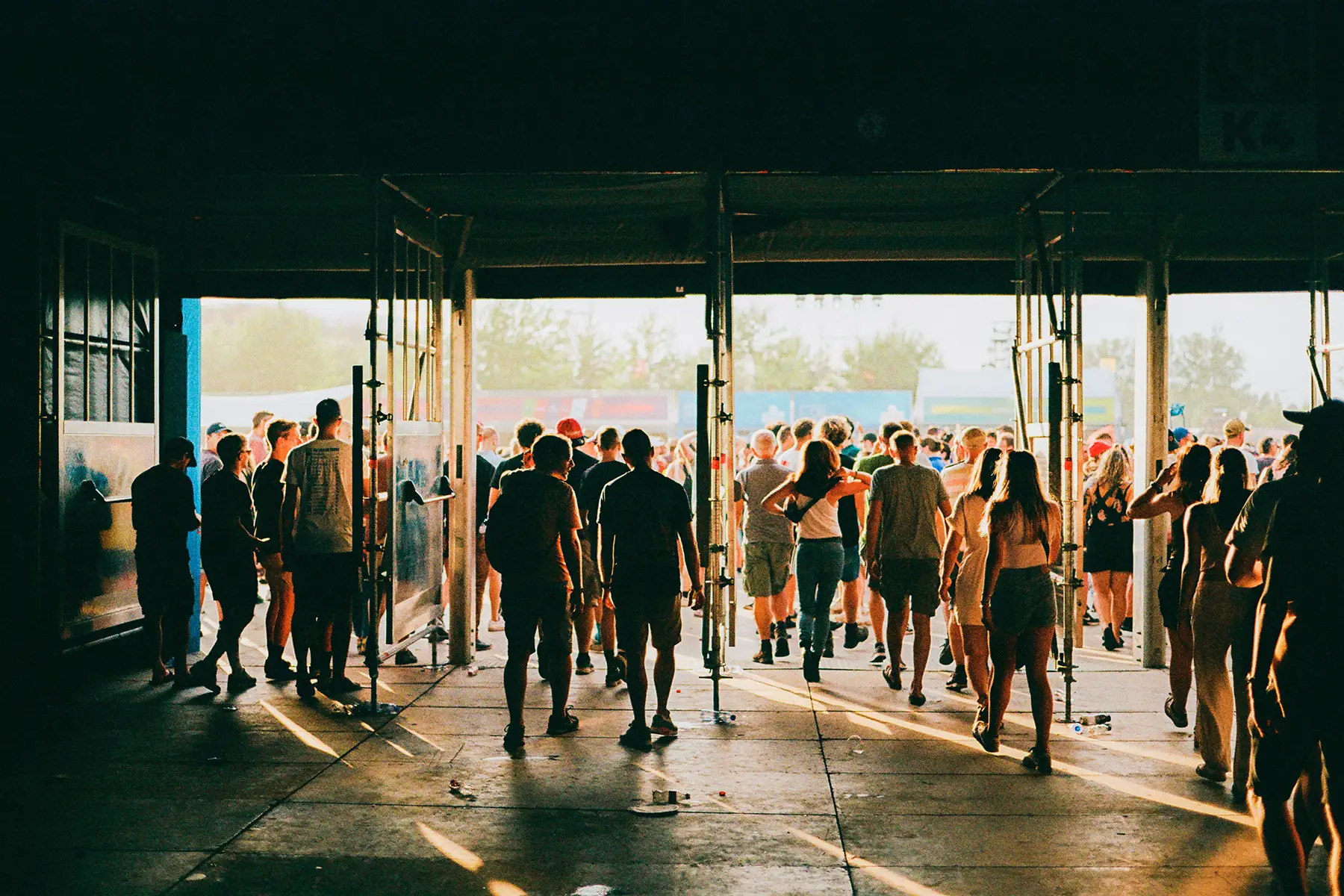 A crowd of people walk through large gates to a festival or large event/market
