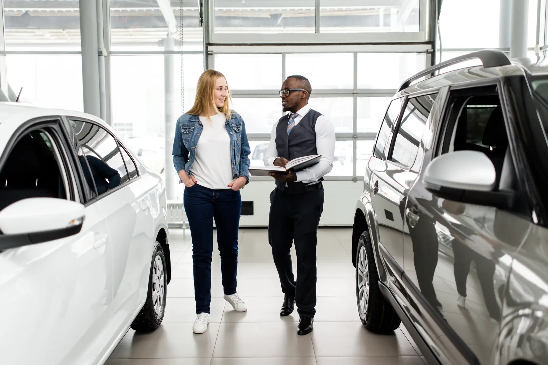 car dealer showing new cars to customer in car showroom