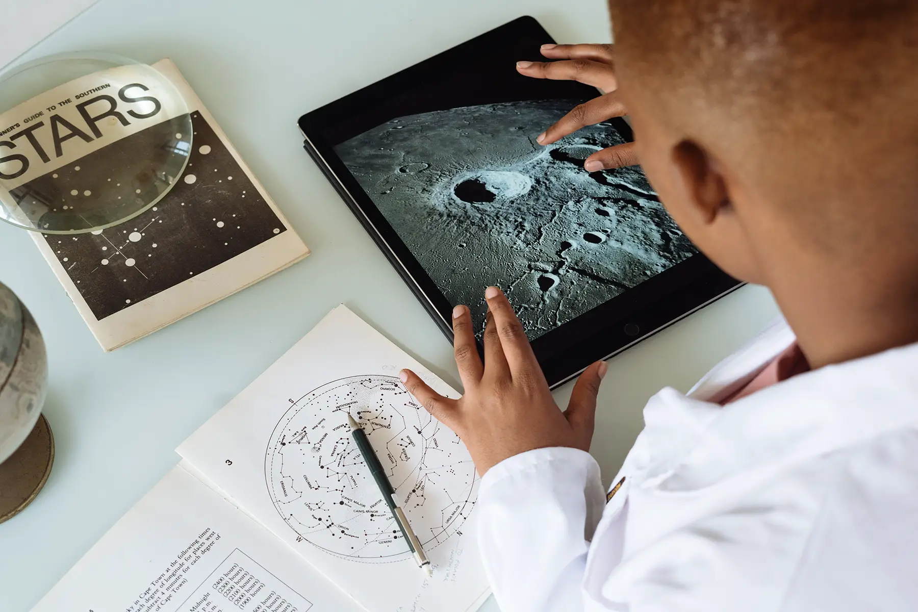 Young boy doing research about the moon, using a tablet and books