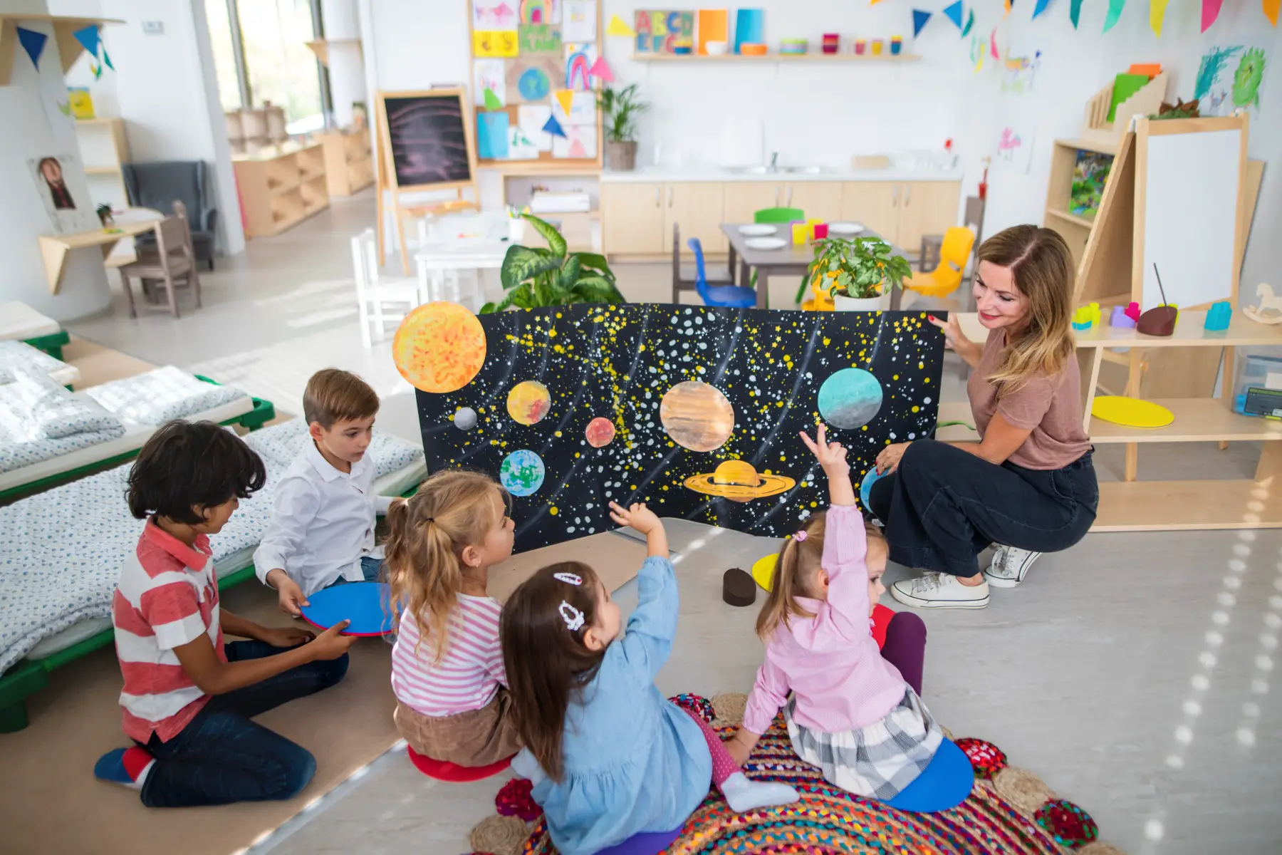a multiracial group of small children sitting on the floor and learning about space with their teacher