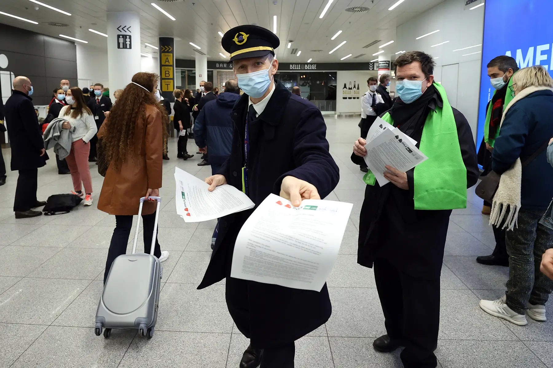 A man in a long jacket, surgical mask, and pilot's cap offers a piece of paper to the photographer. Workers on strike.