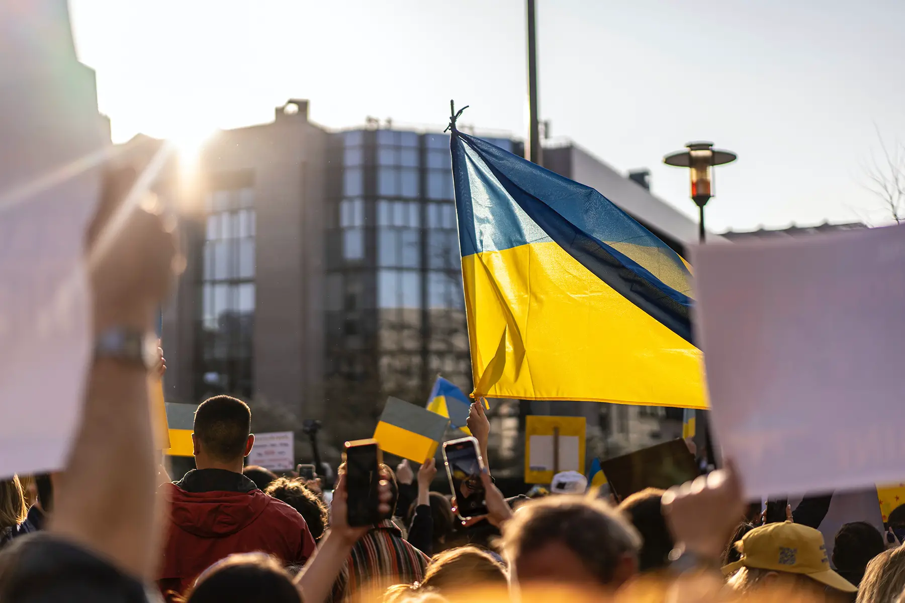 A crowd holding Ukraine flags protests outside a glass building