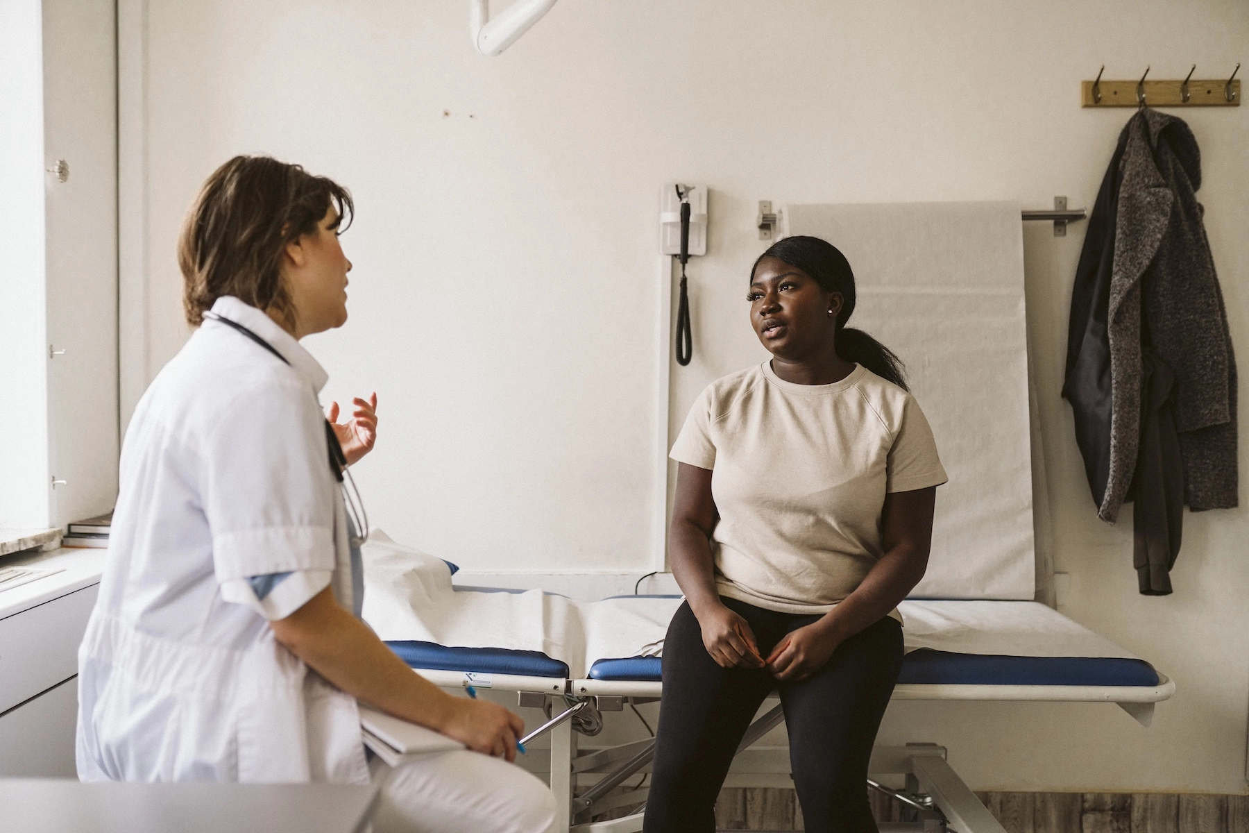 A doctor speaks with her female patient as they sit across from each other in the examination room