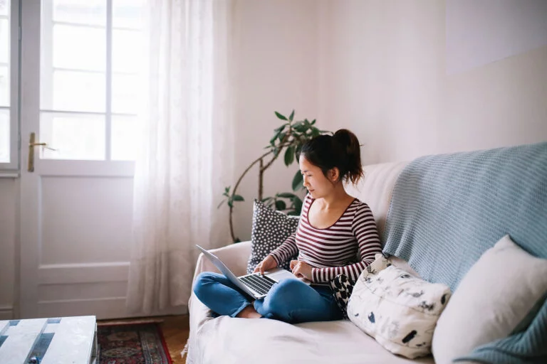 Woman sitting on the couch at home, reading thew news on her laptop.