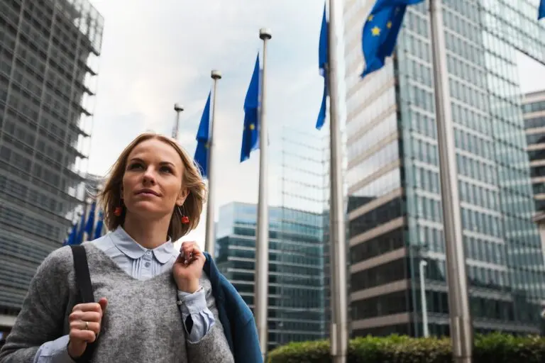 Woman walking in front of the European Union offices in Brussels with EU Flags flying in the background.