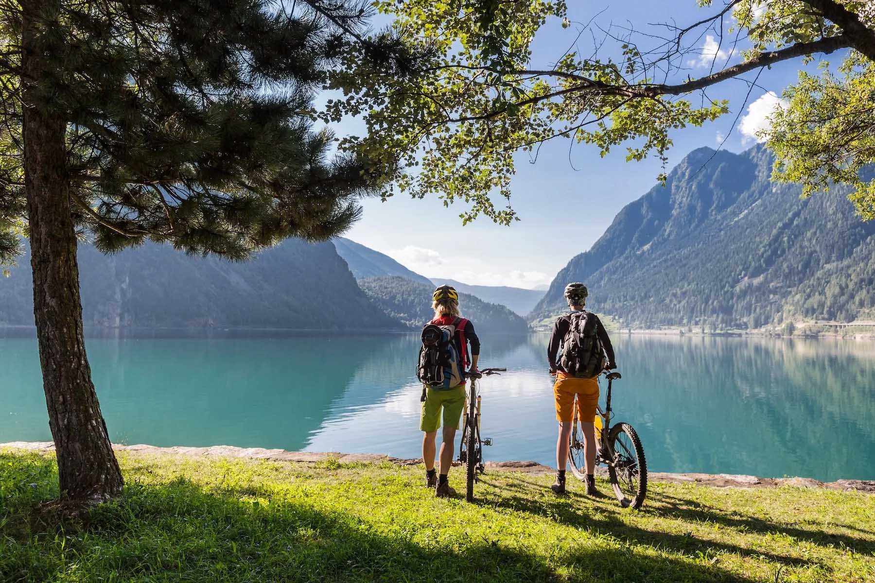Two mountain bikers stand with their bicycles looking out over lake Poschiavo, Graubünden, Switzerland