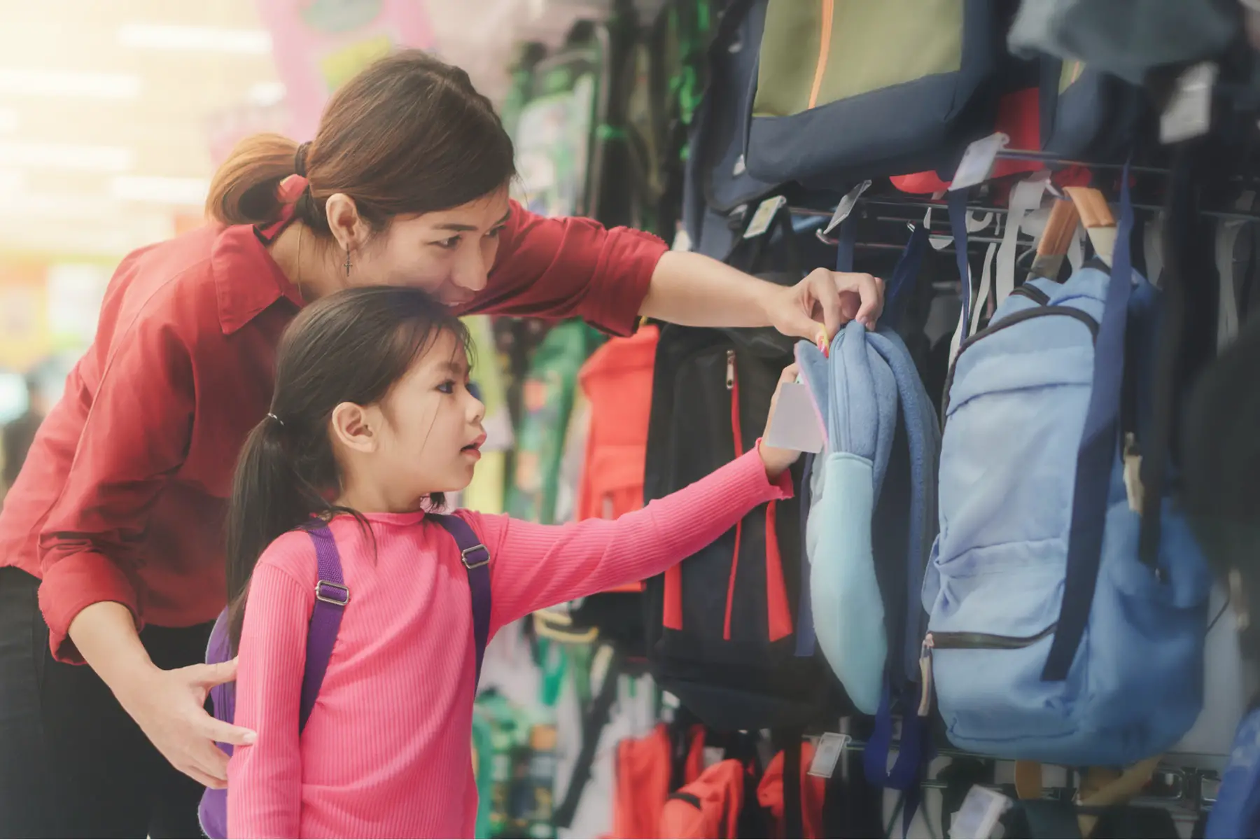 Mom helps daughter hang up school bag at the hooks outside class