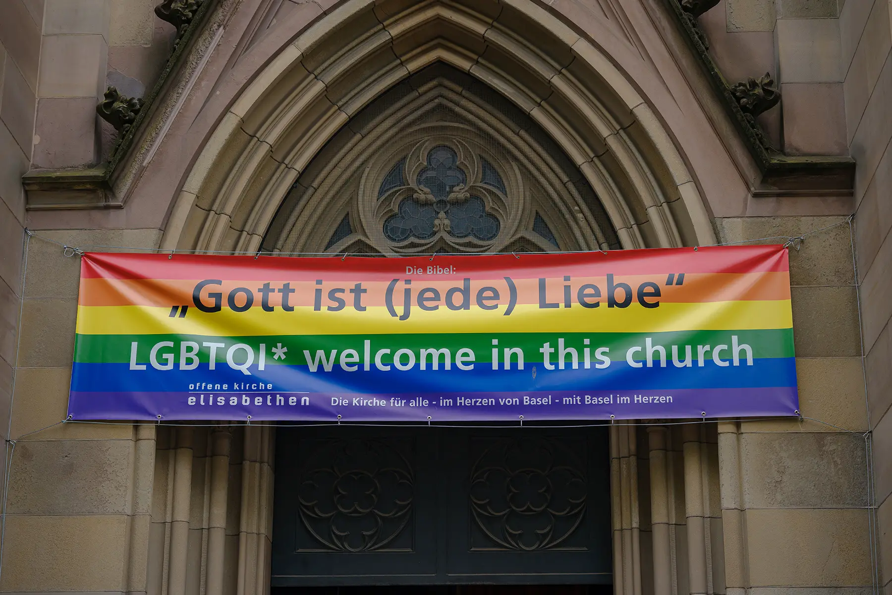 A church door with a pride flag banner which reads 