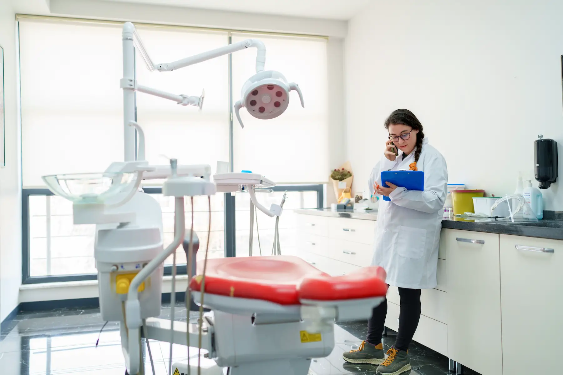 A female dentist stands in the exam room holding a patient's chart while on the phone