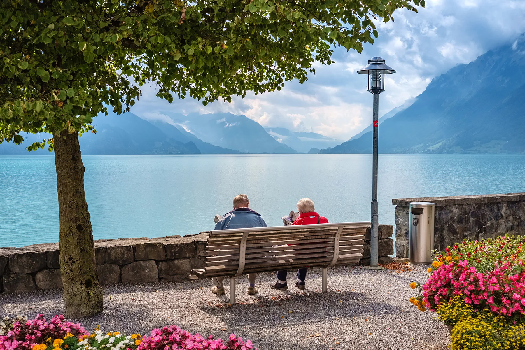 Elderly couple reading newspapers on bench in Brienz