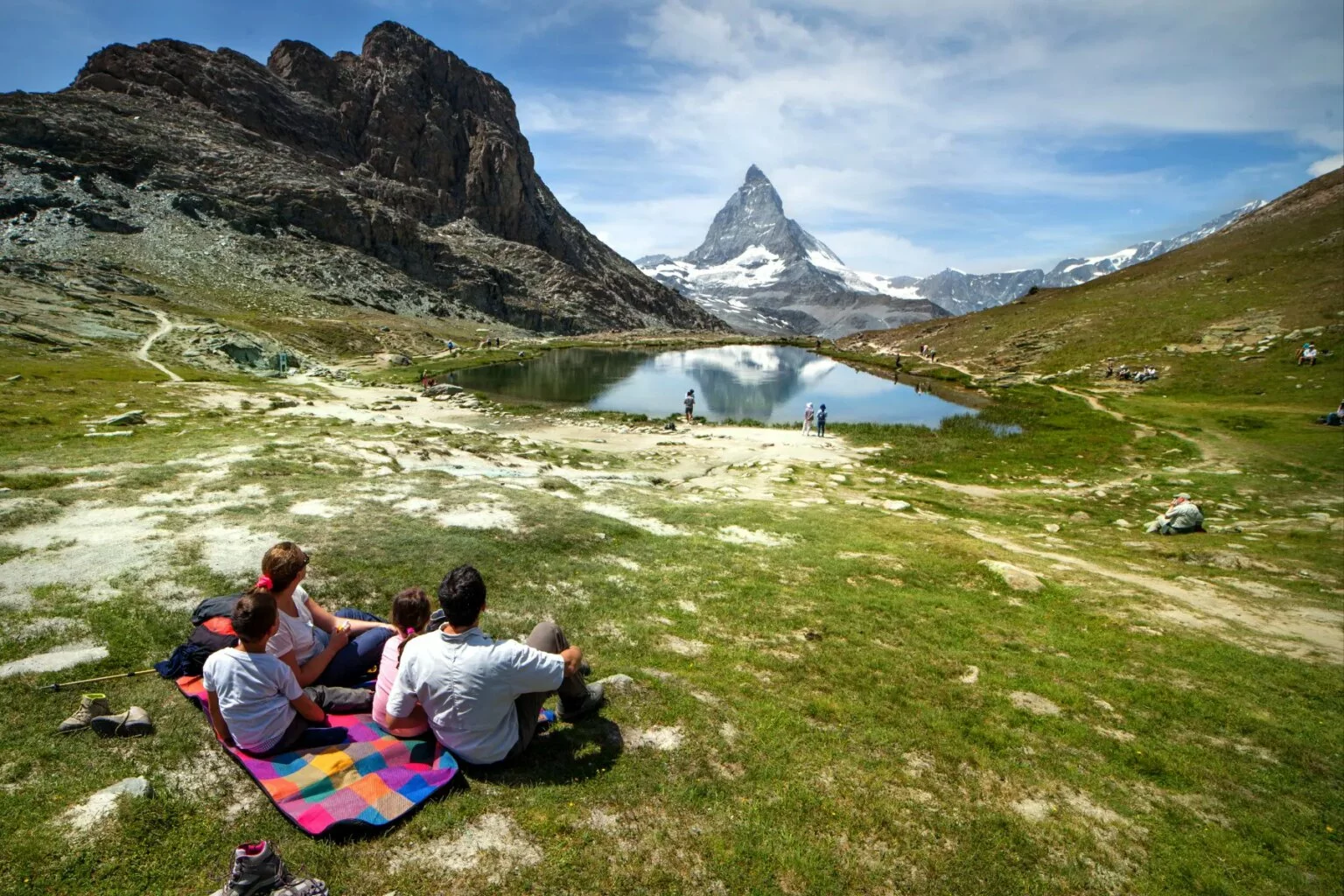 Family of four sitting on picnic mat looking at Matterhorn mountain and lake.