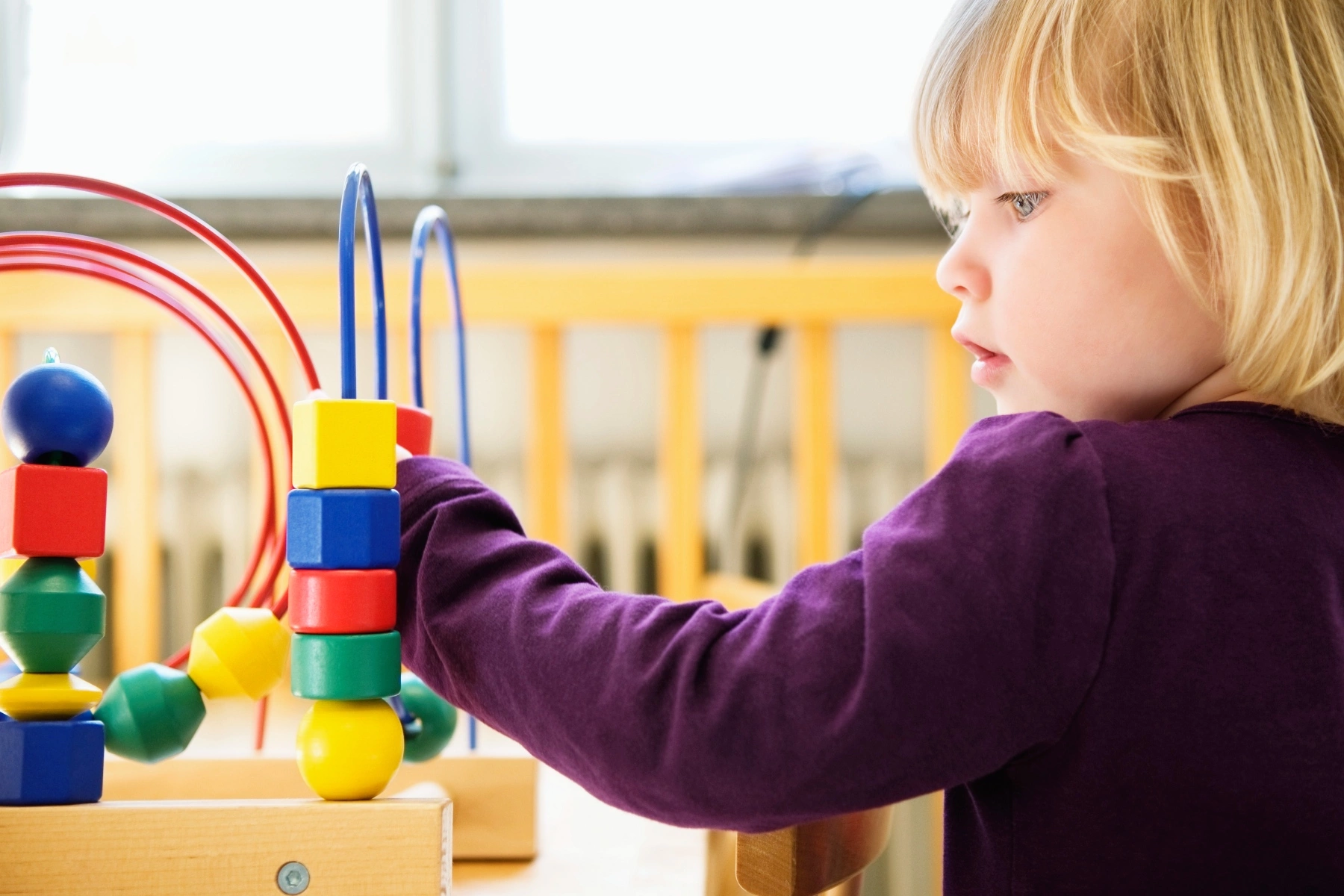 a side shot of a little blonde girl playing with a bead maze in a daycare setting