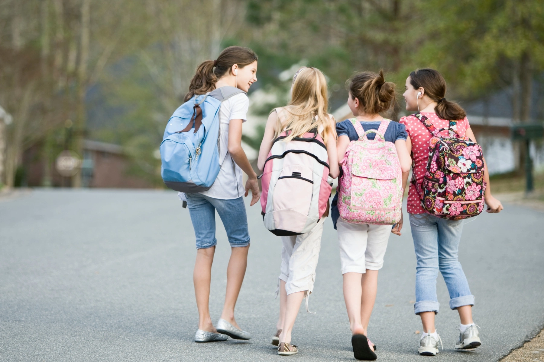 four young girls walking together in a row away from the camera wearing backpacks