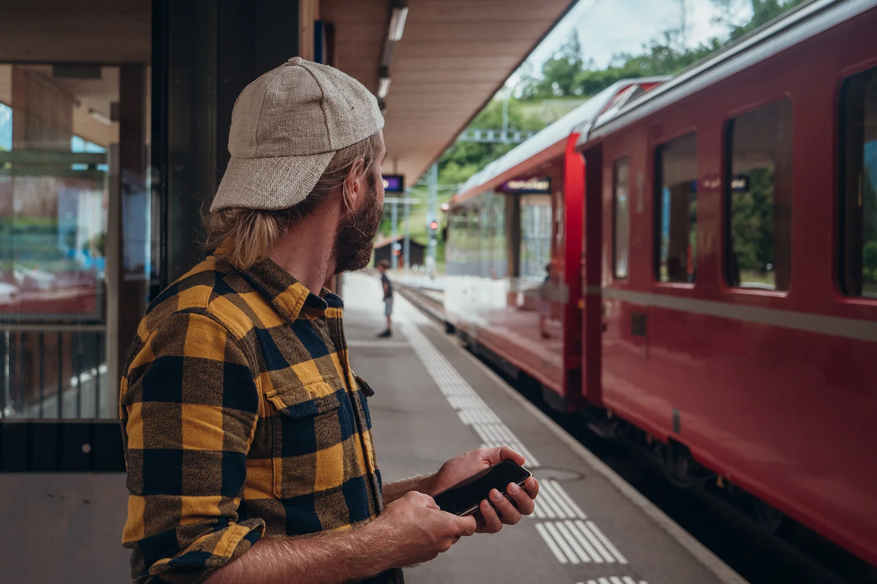 Man holding his phone on a train station platform in Switzerland