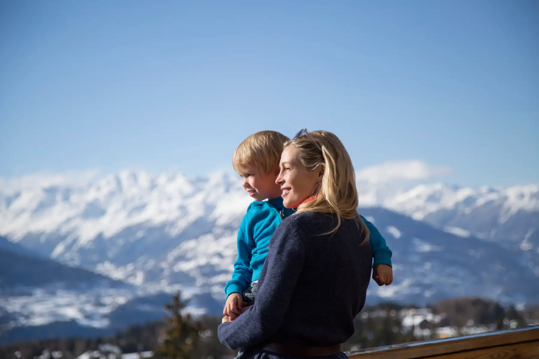 a side profile shot of a blonde woman holding a little boy with the Swiss Alps in the background