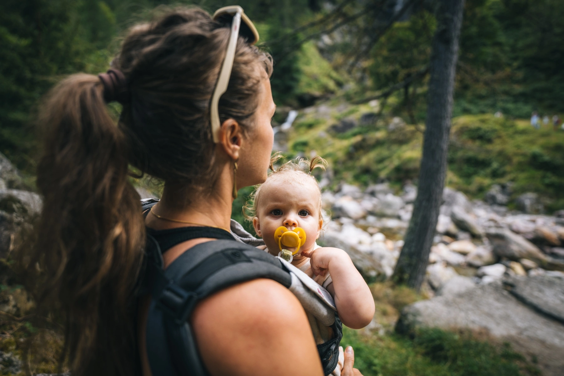 Child with pacifier strapped to mother's chest during forest walk