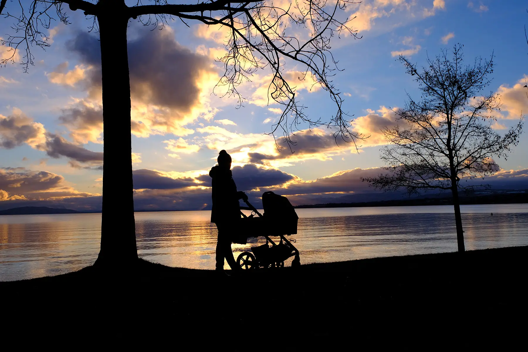 Black silhouette of a parent strolling along the banks of Lake Geneva at sunset with a baby in the stroller