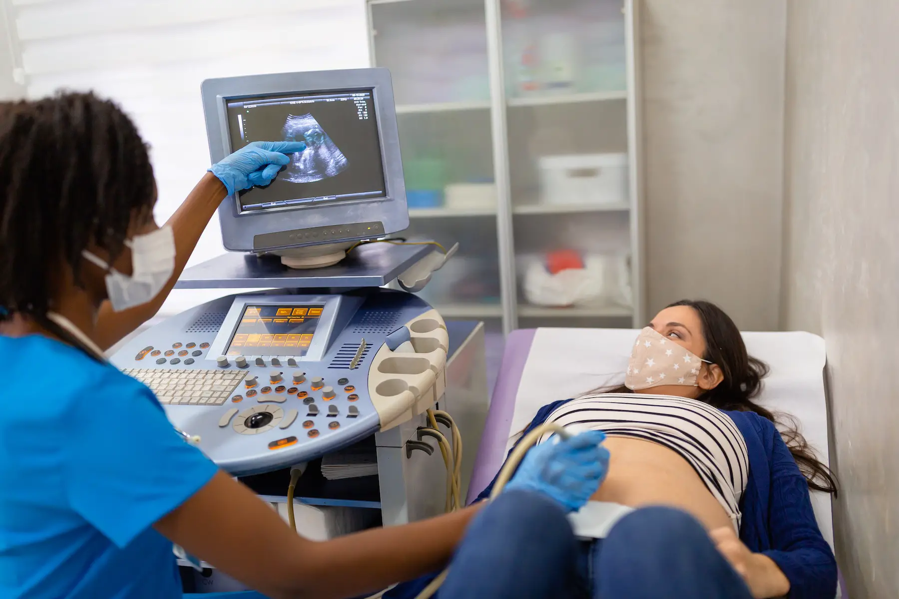 A female technician doing an ultrasound examination of a pregnant woman who is lying back on the exam table
