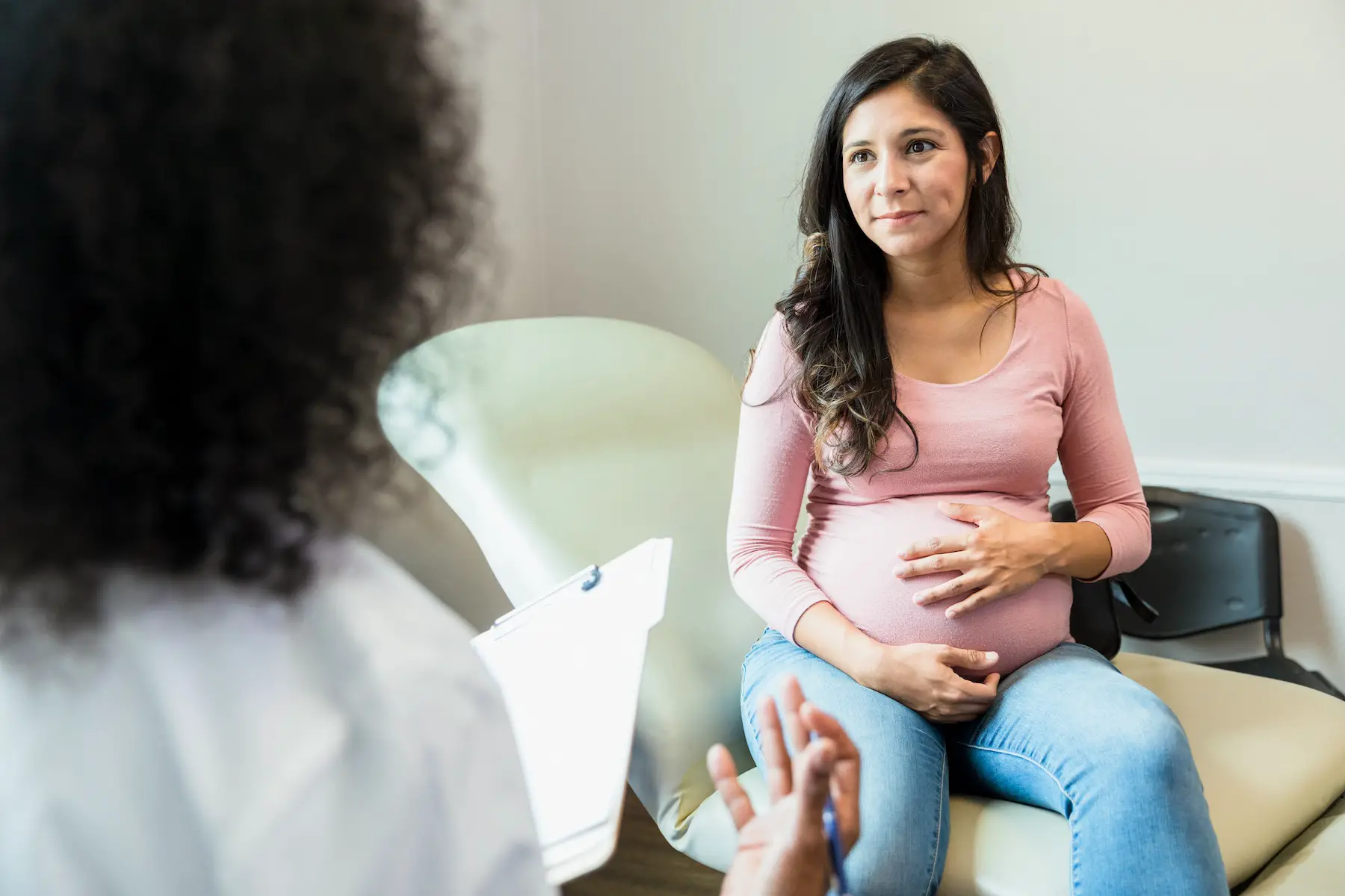 Pregnant woman touches her baby bump as she listens to a doctor talking and holding her medical records