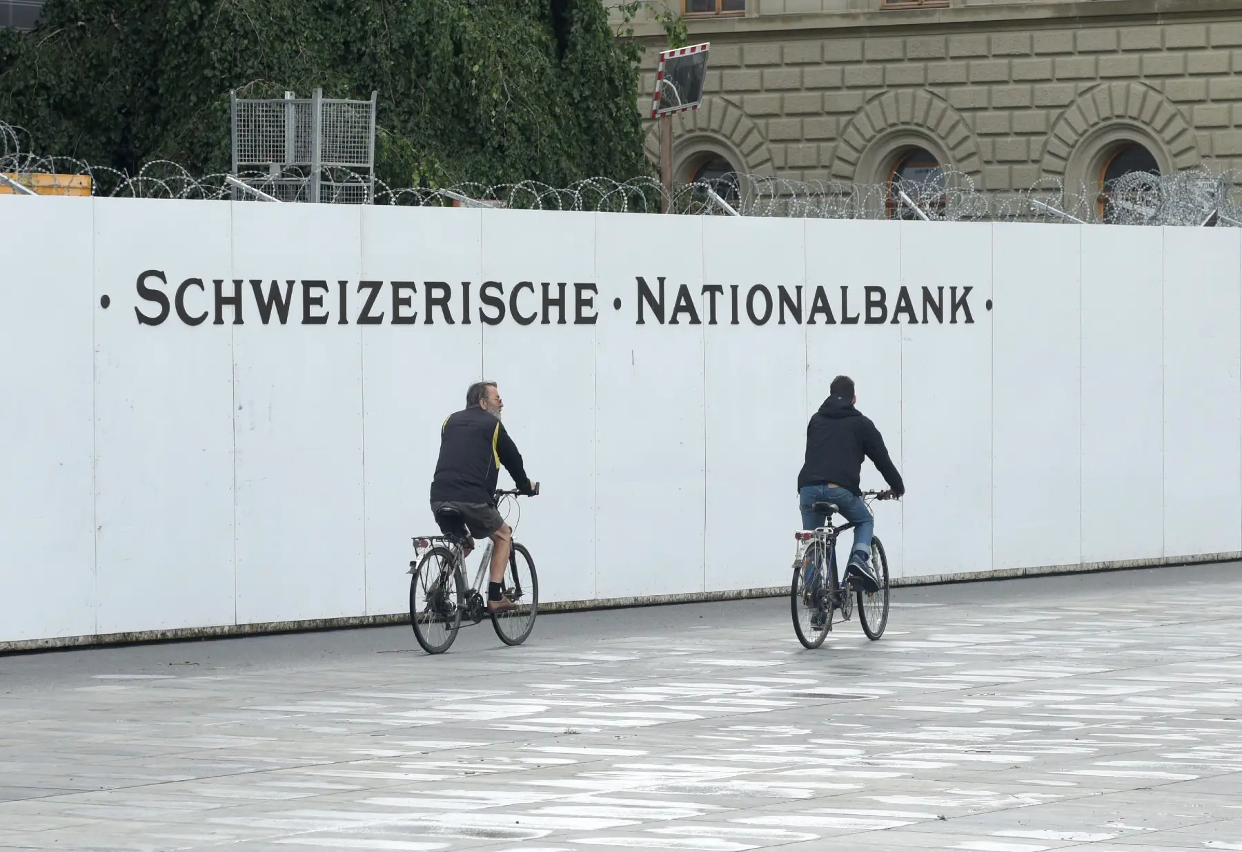 cyclists ride by the Swiss National bank sign, why is Switzerland so rich