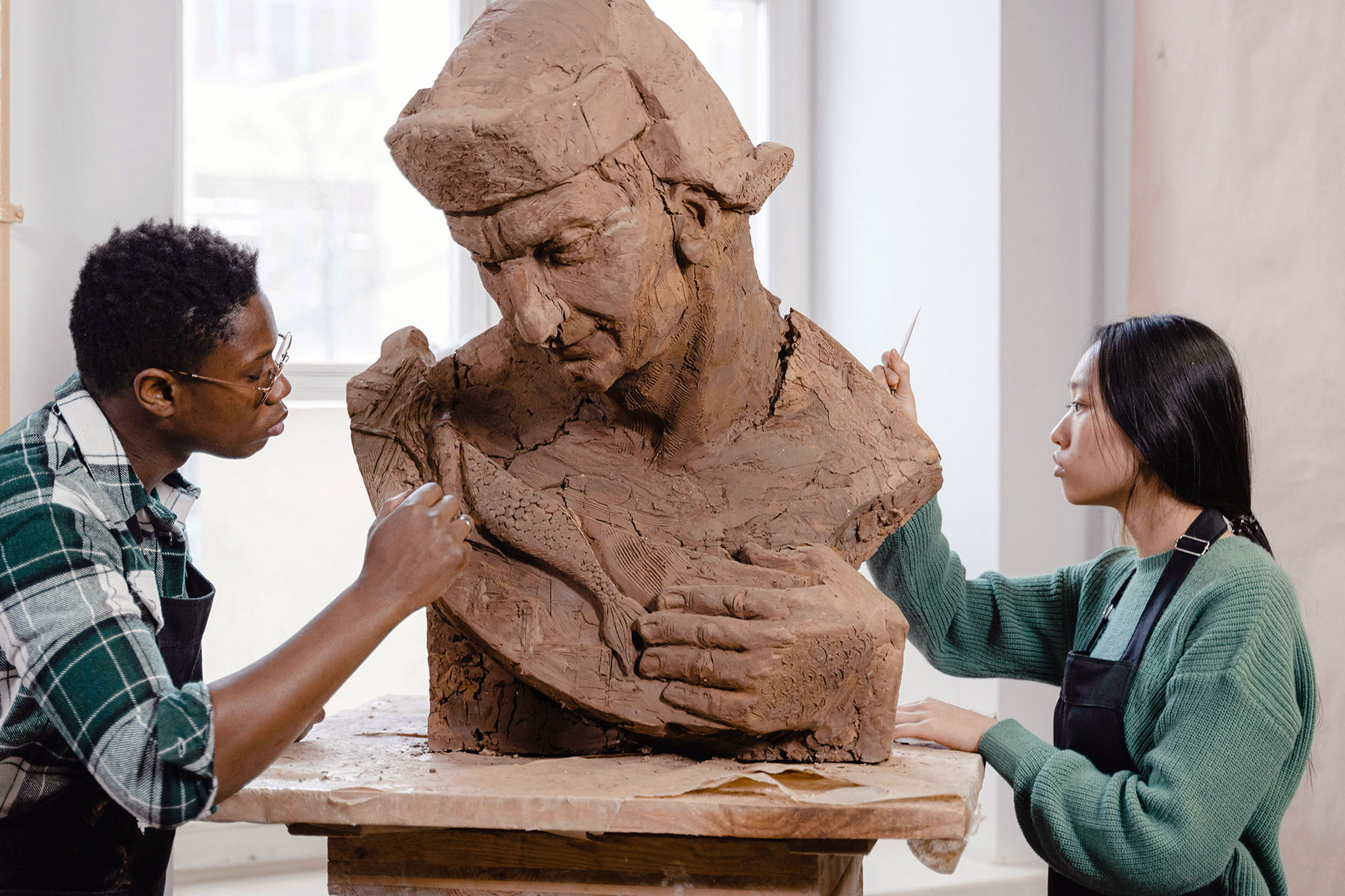 Two sculptors crafting a clay sculpture. They're very concentrated at work.