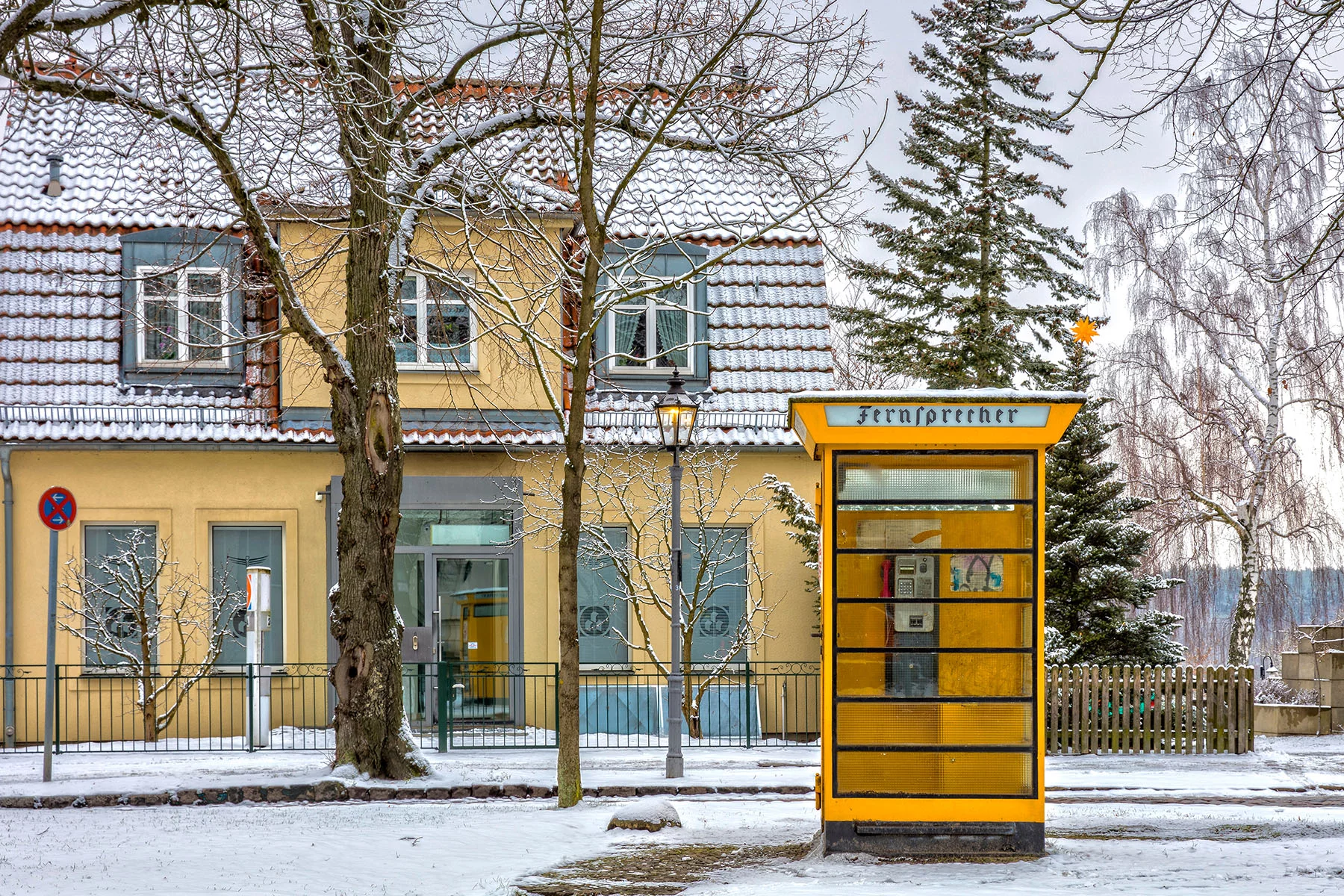 A yellow telephone box in front of a yellow house in the snow in Reinickendorf, Berlin
