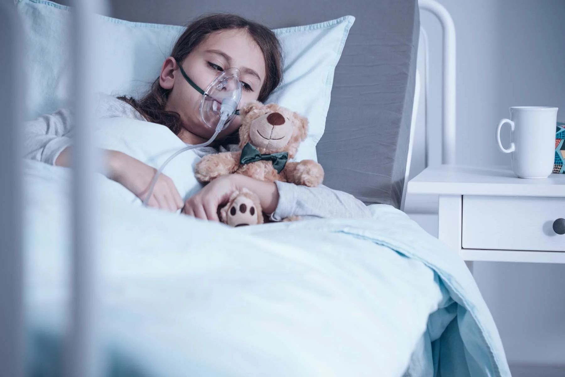 child sick in hospital bed with teddy bear