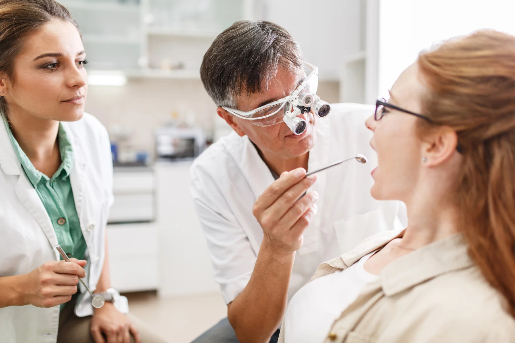 Dentist with specialized glasses and assistant examine patient's teeth