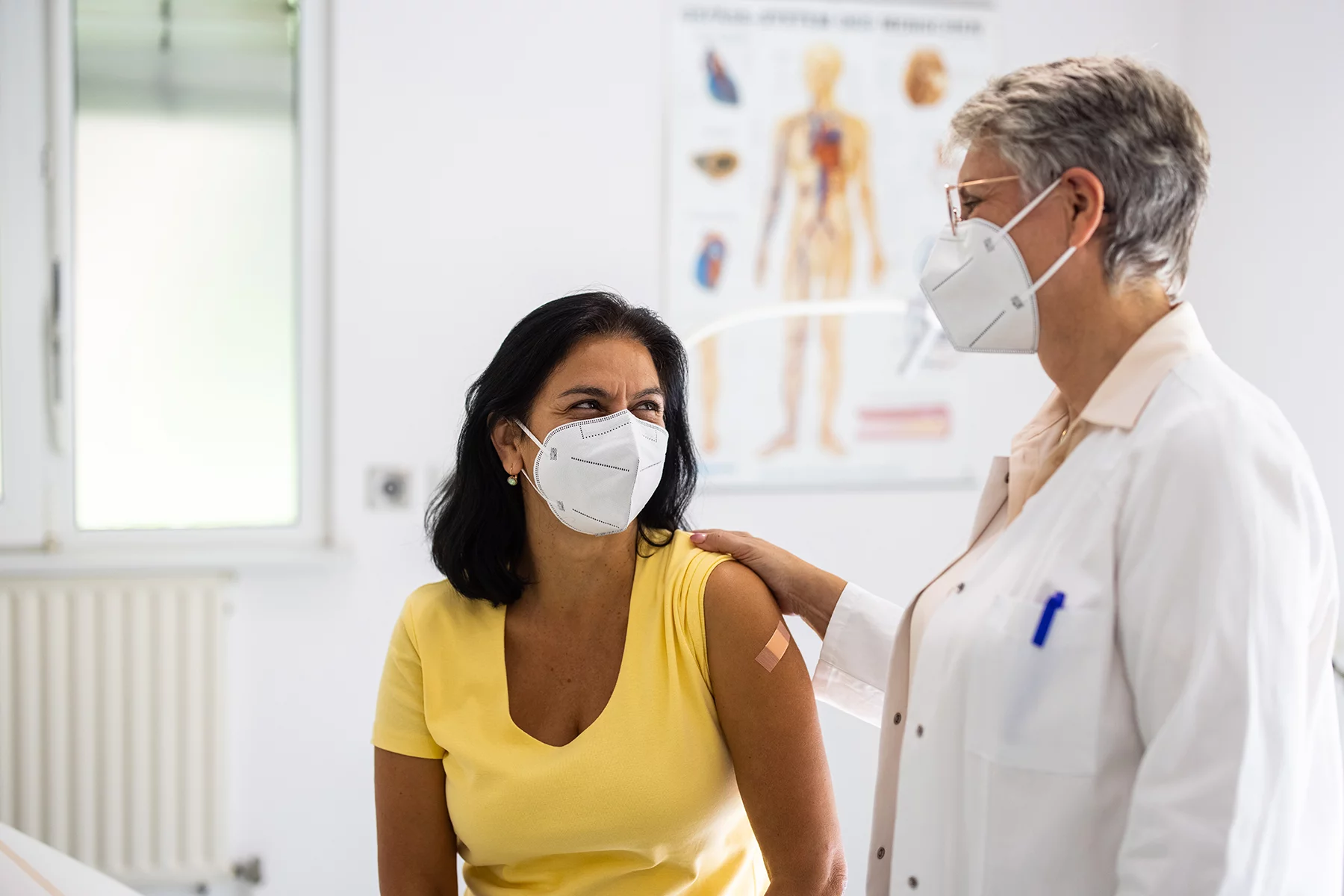 A doctor touching her patient's shoulder. Both wearing FFP2 masks.