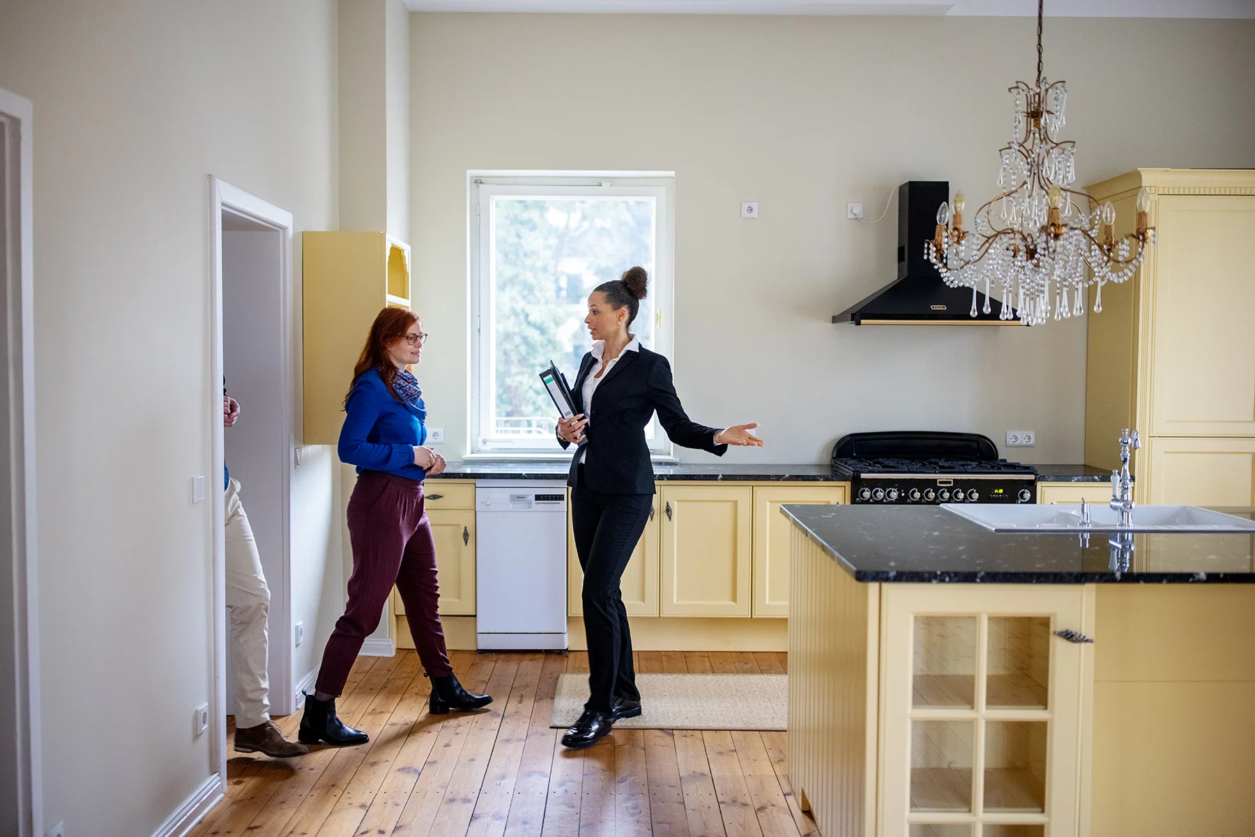 An estate agent shows a couple around a white and yellow kitchen