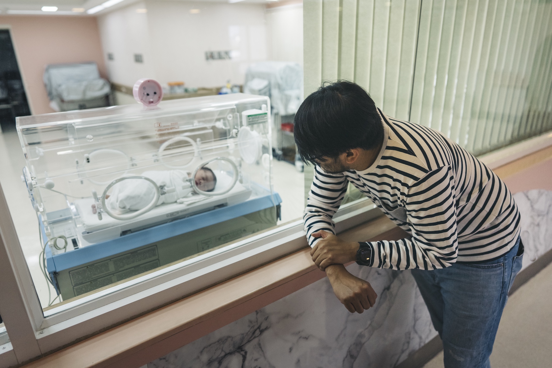 A father looks through the window of a hospital's neonatal unit where his baby sleeps in an incubator