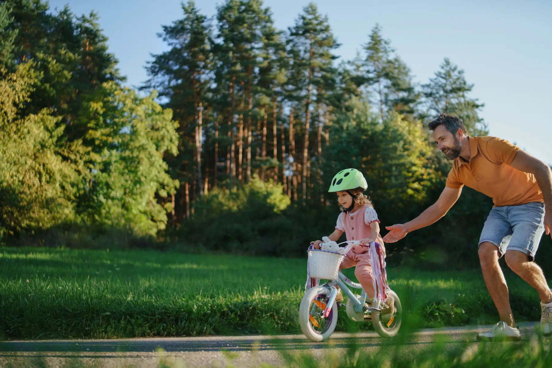 a little girl wearing a cycling helmet and getting support from her father when riding a bike for the first time