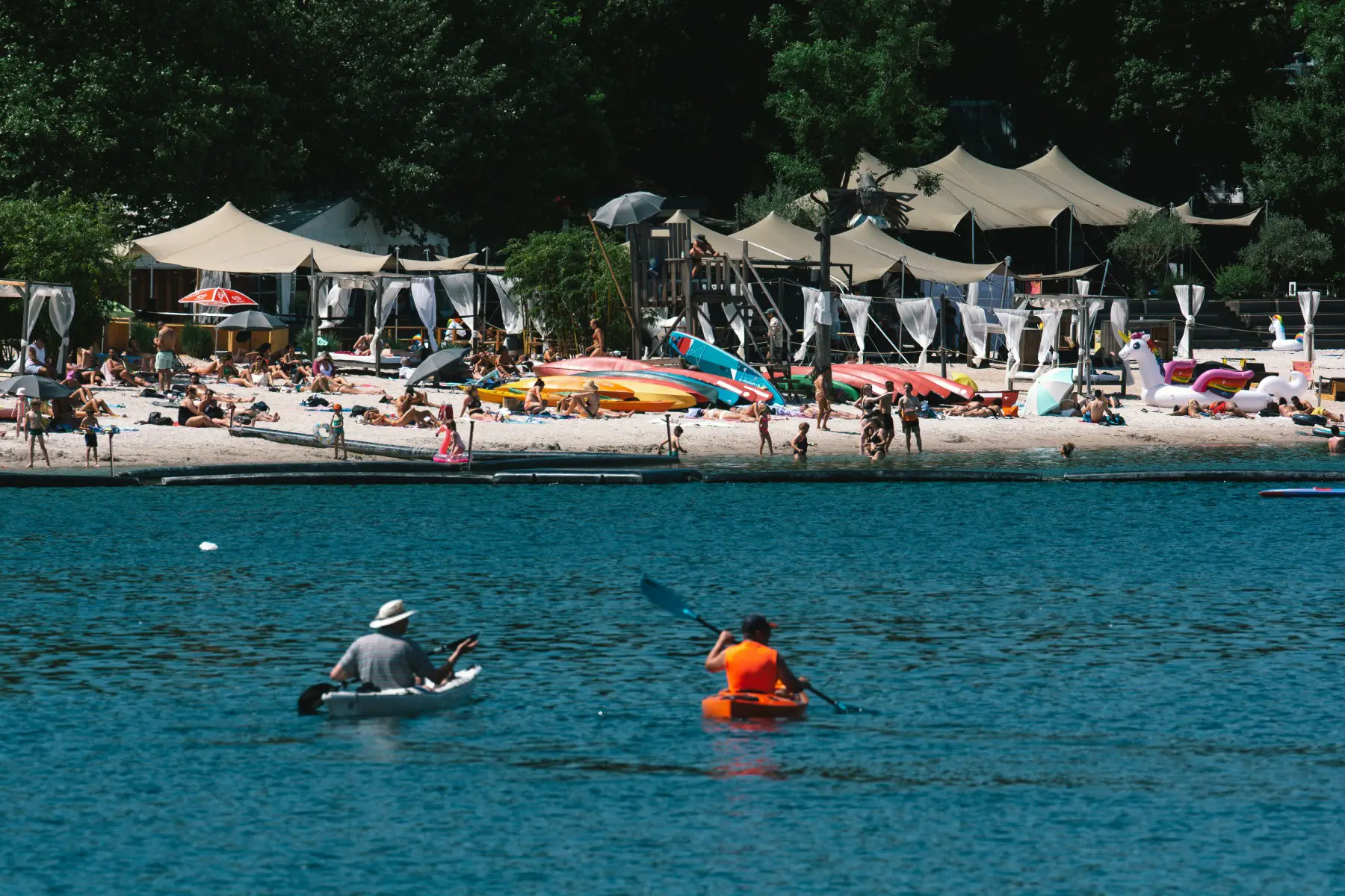 people relaxing in the sun at Fühlinger See beach on a summer day in Cologne, with two people kayaking in the foreground