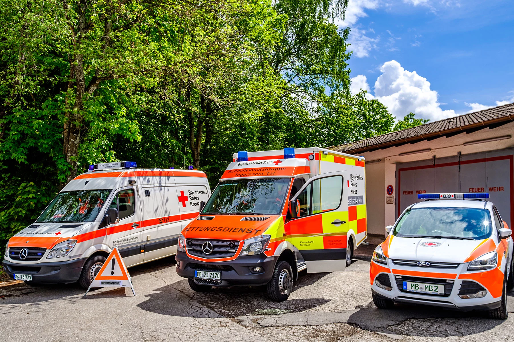 Three different types of German emergency vehicles are parked outside on a sunny day
