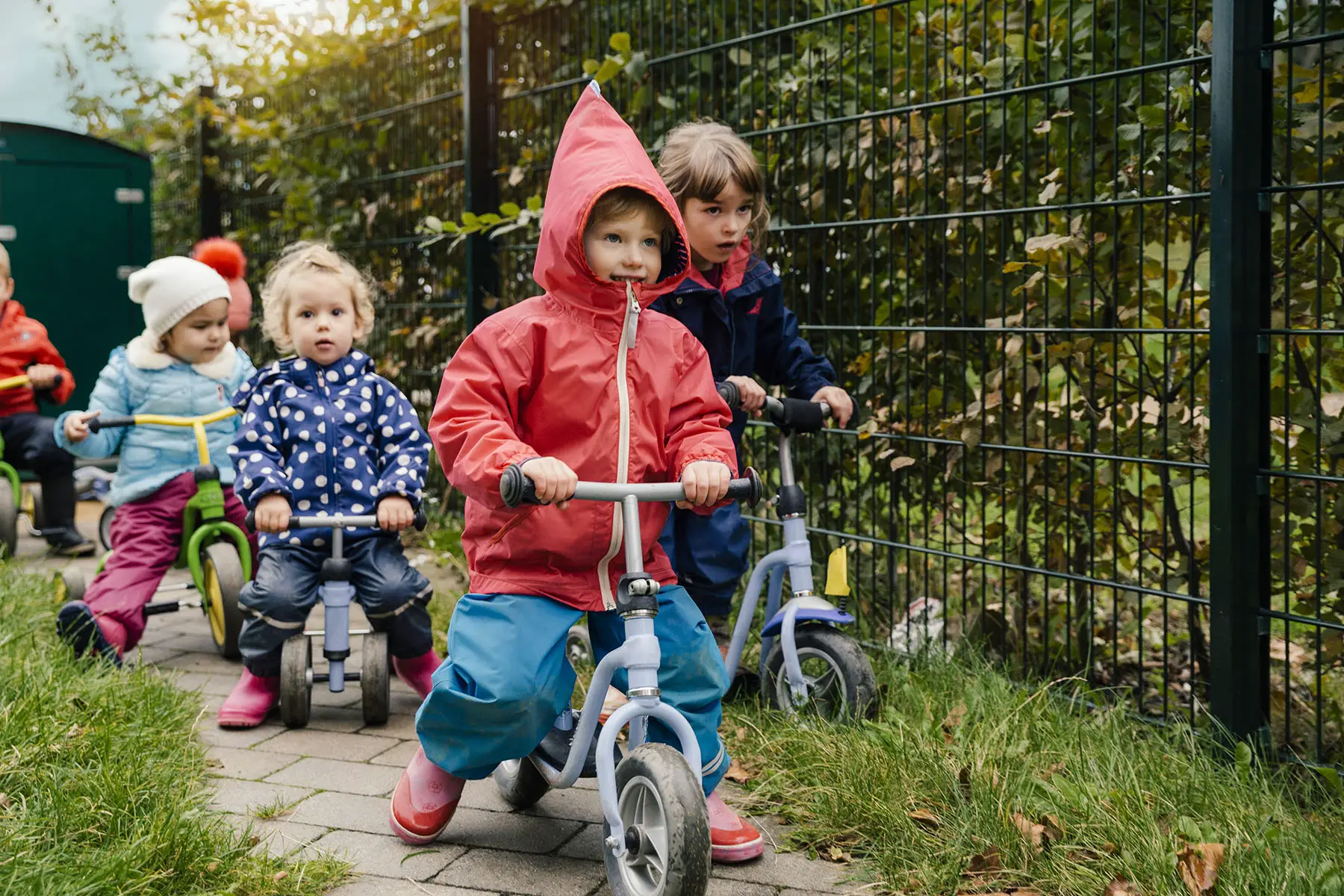 Group of children using walking bicycles in a garden of a daycare center.